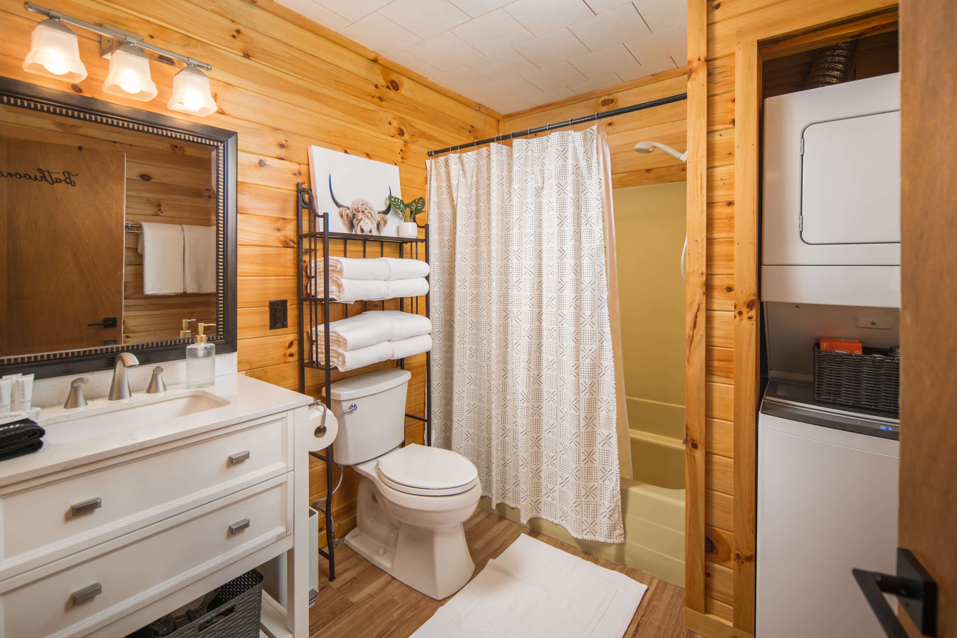 A wooden-paneled bathroom featuring a shower, toilet, sink with a mirror, and a stacked washer and dryer.