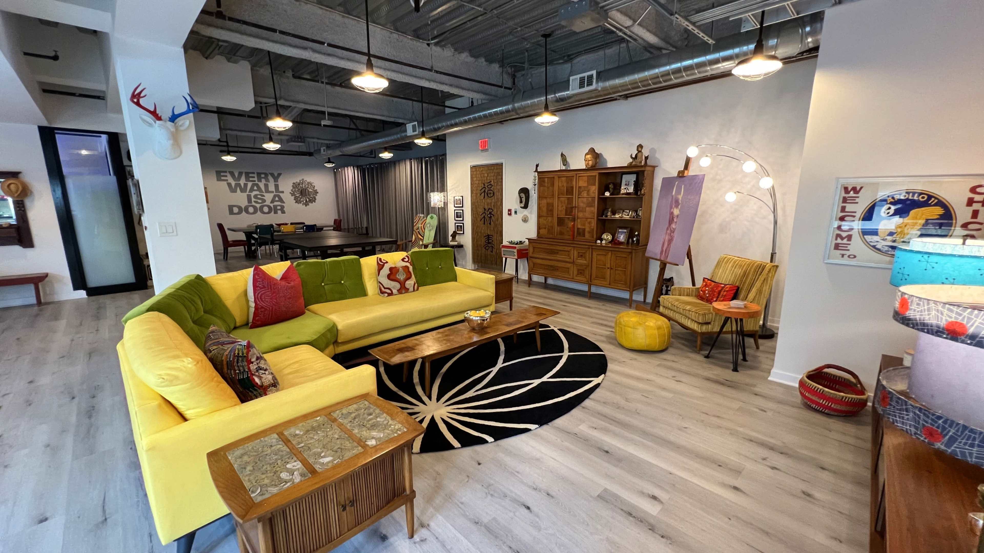 The image shows a modern living room with a yellow sectional sofa, a round black and white rug, a wooden coffee table, and various decorative items, including a cabinet and chairs.