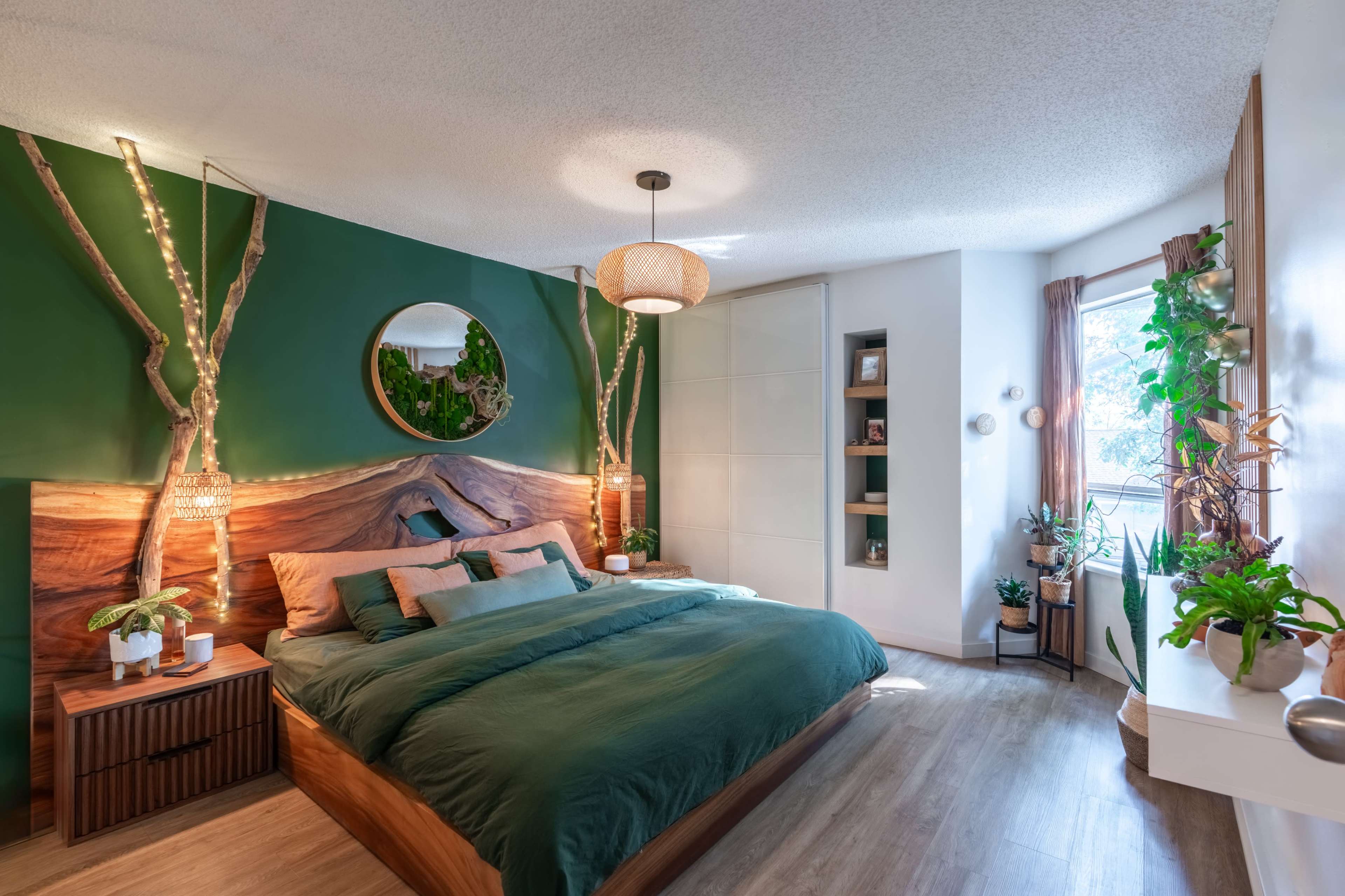 The image shows a modern bedroom with a green accent wall, a wooden bed frame, decorative plants, and natural elements integrated into the design.