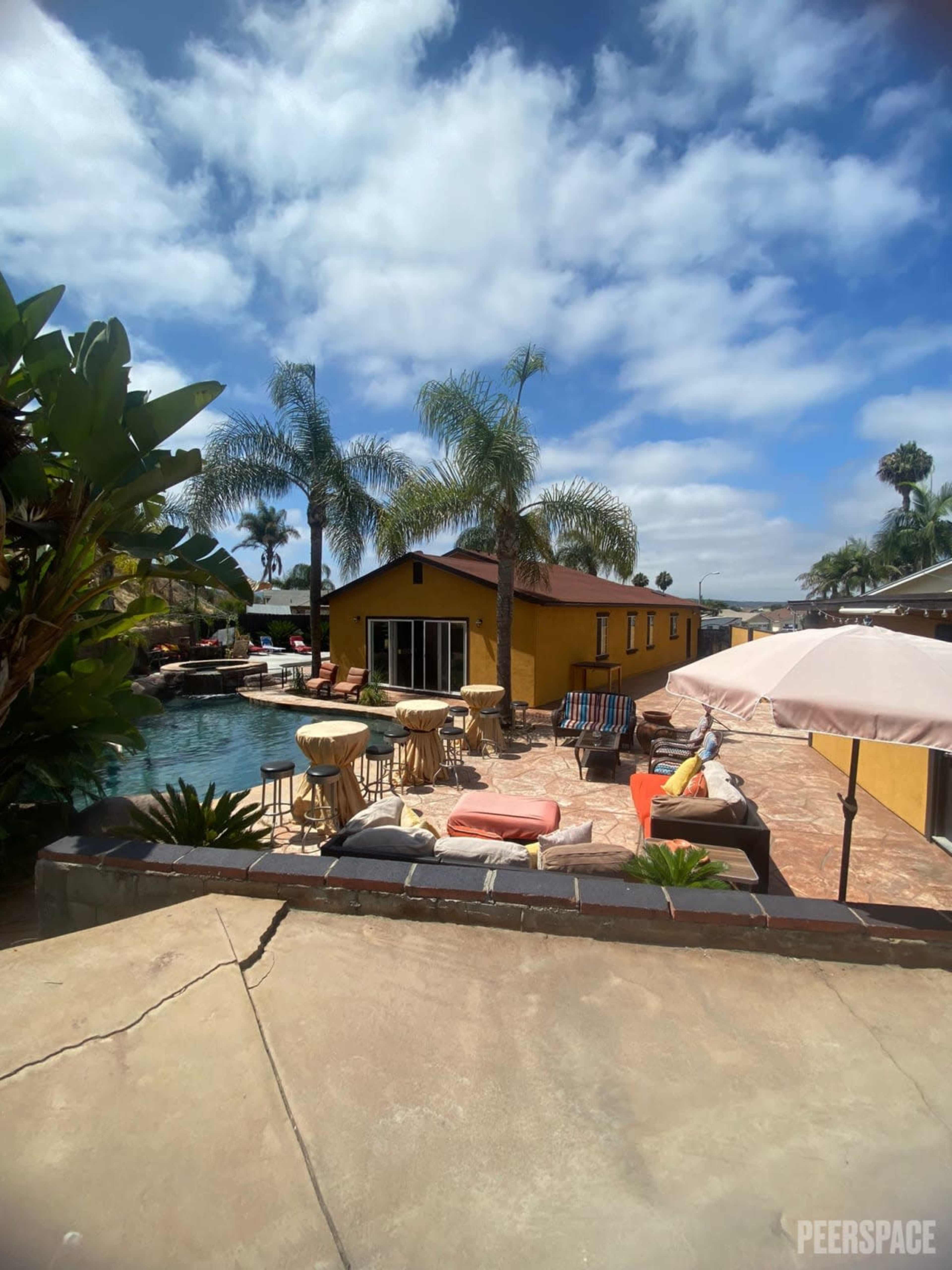 A sunny outdoor pool area with palm trees, lounge chairs, and a yellow building in the background.