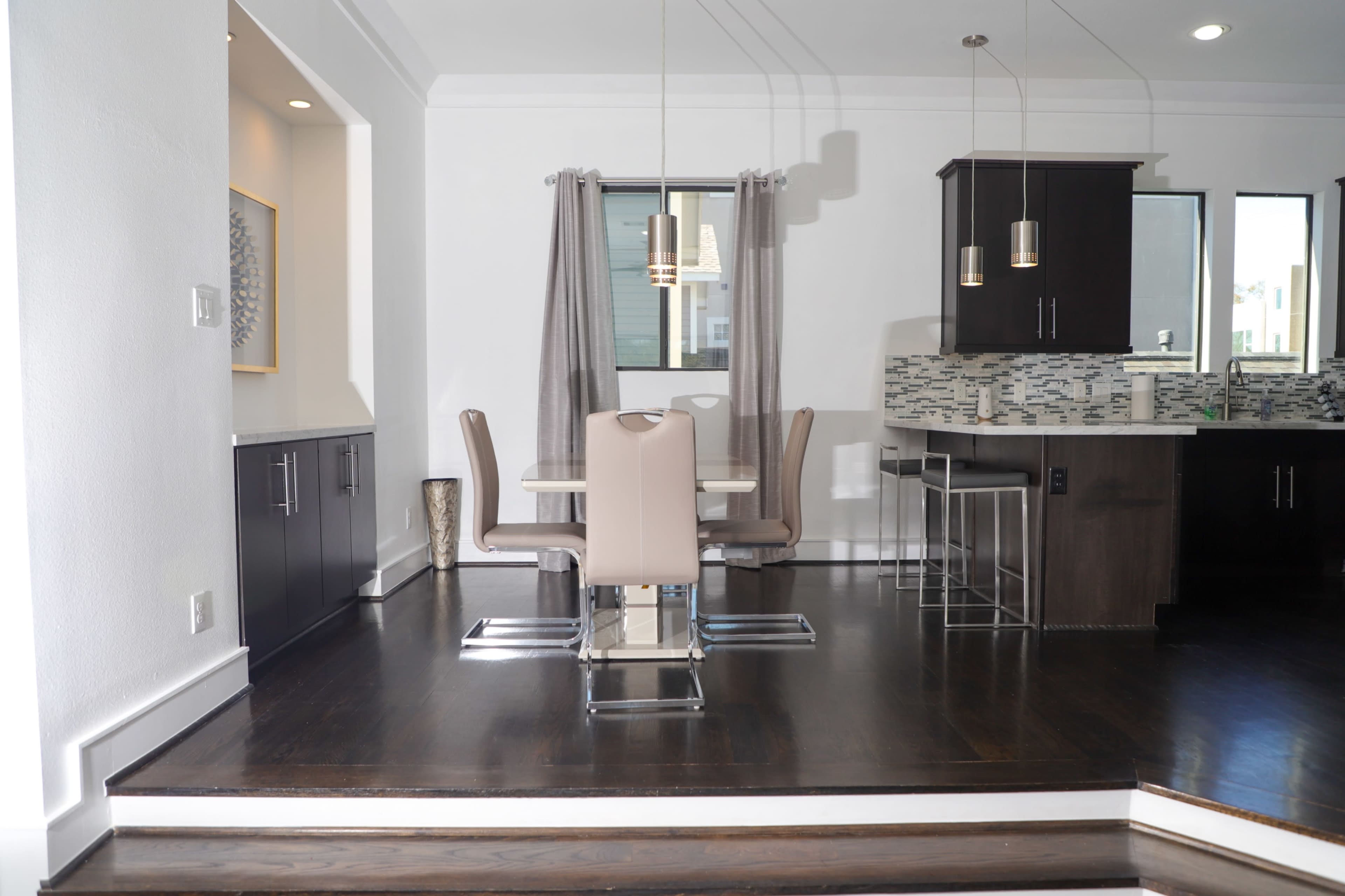 A modern kitchen and dining area with a table and chairs, sleek cabinetry, and pendant lighting.