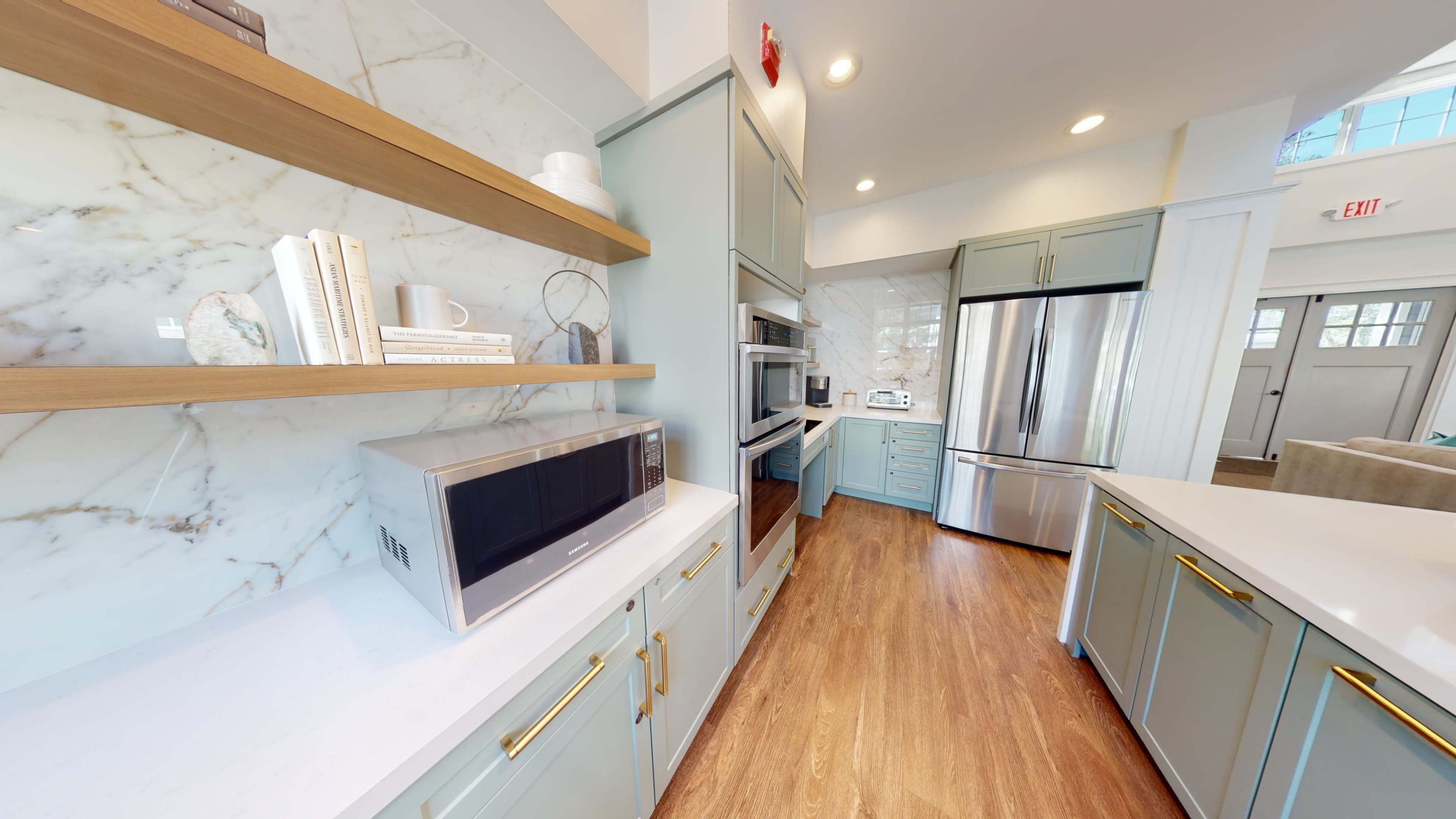 A modern kitchen features light green cabinetry, a stainless steel refrigerator, and marble-patterned backsplash with open shelving.
