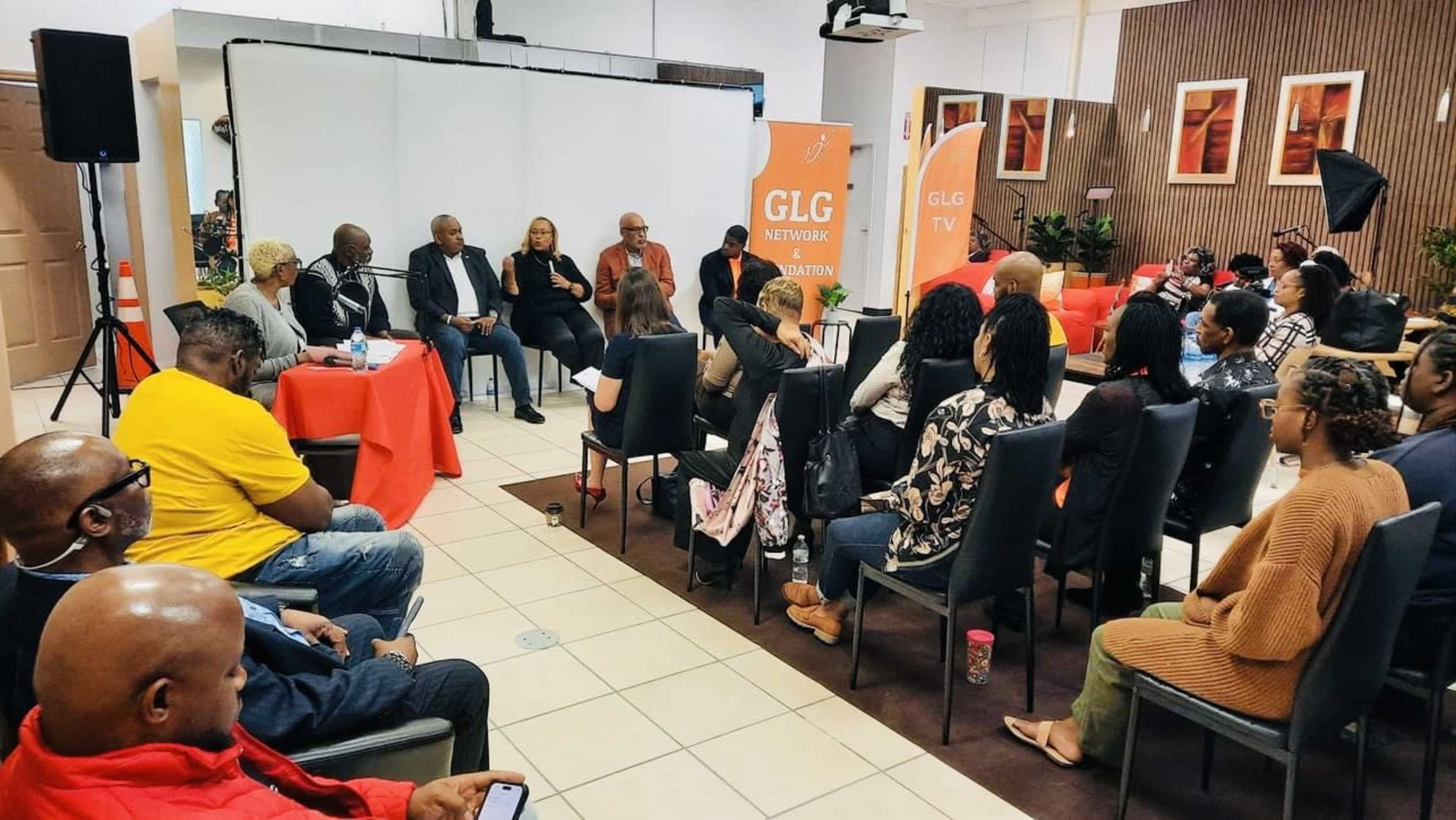 A panel discussion is taking place in a room with audience members seated and facing a group of speakers at the front.