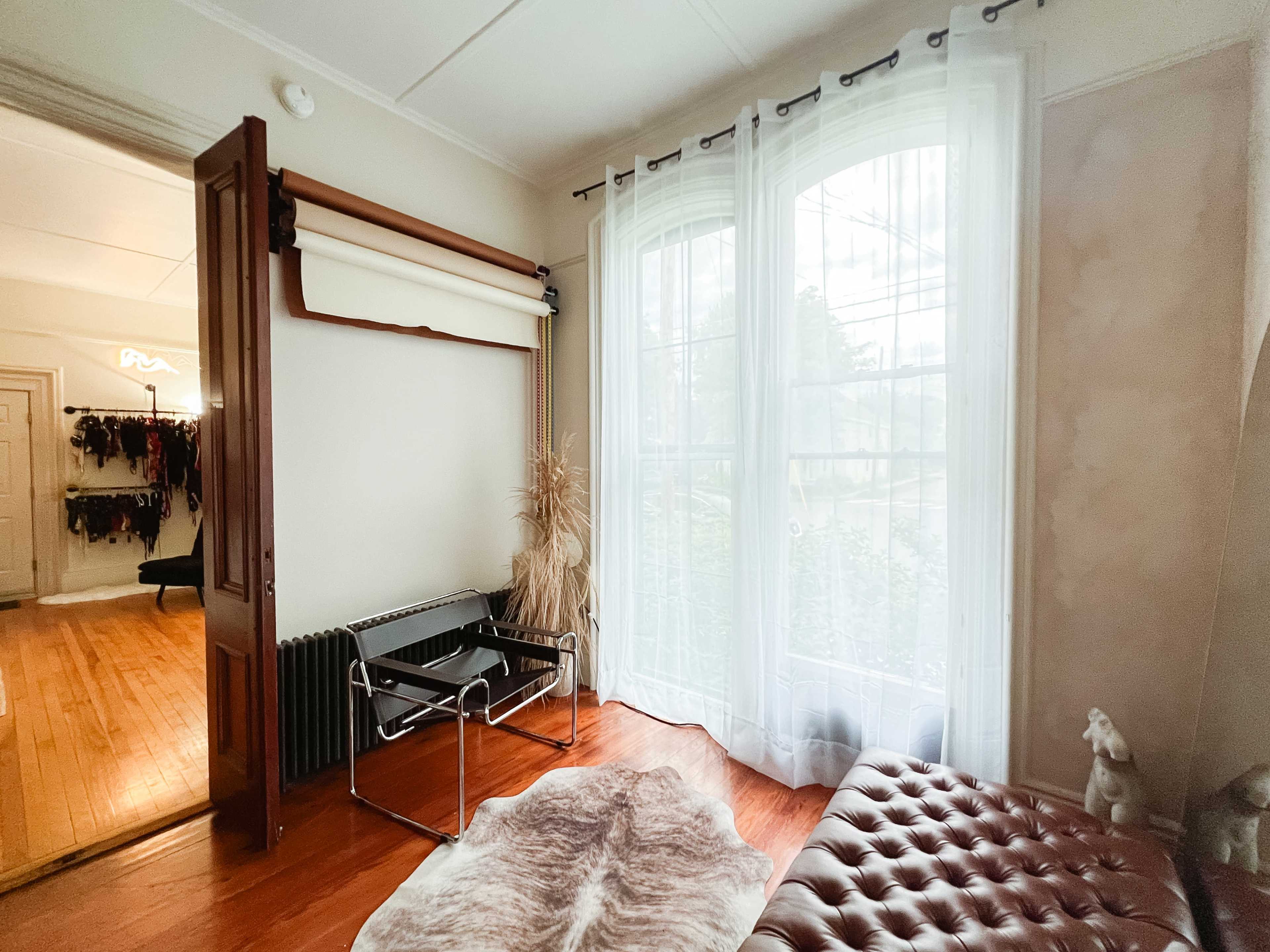 The room features a chair by a large window, a thin rug on the wooden floor, and a door leading to another space.