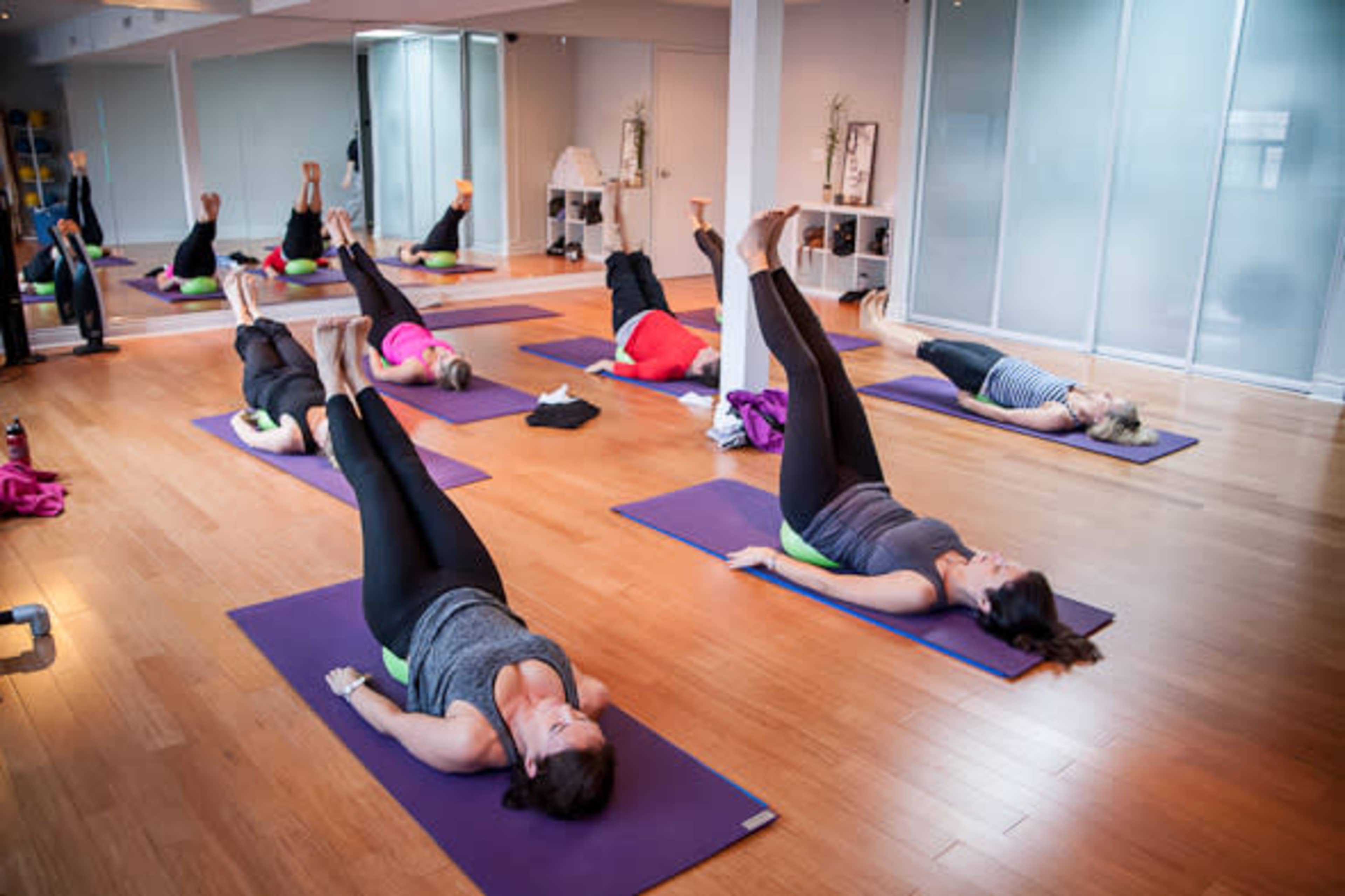Several people are practicing a yoga pose on mats in a spacious studio with natural light.