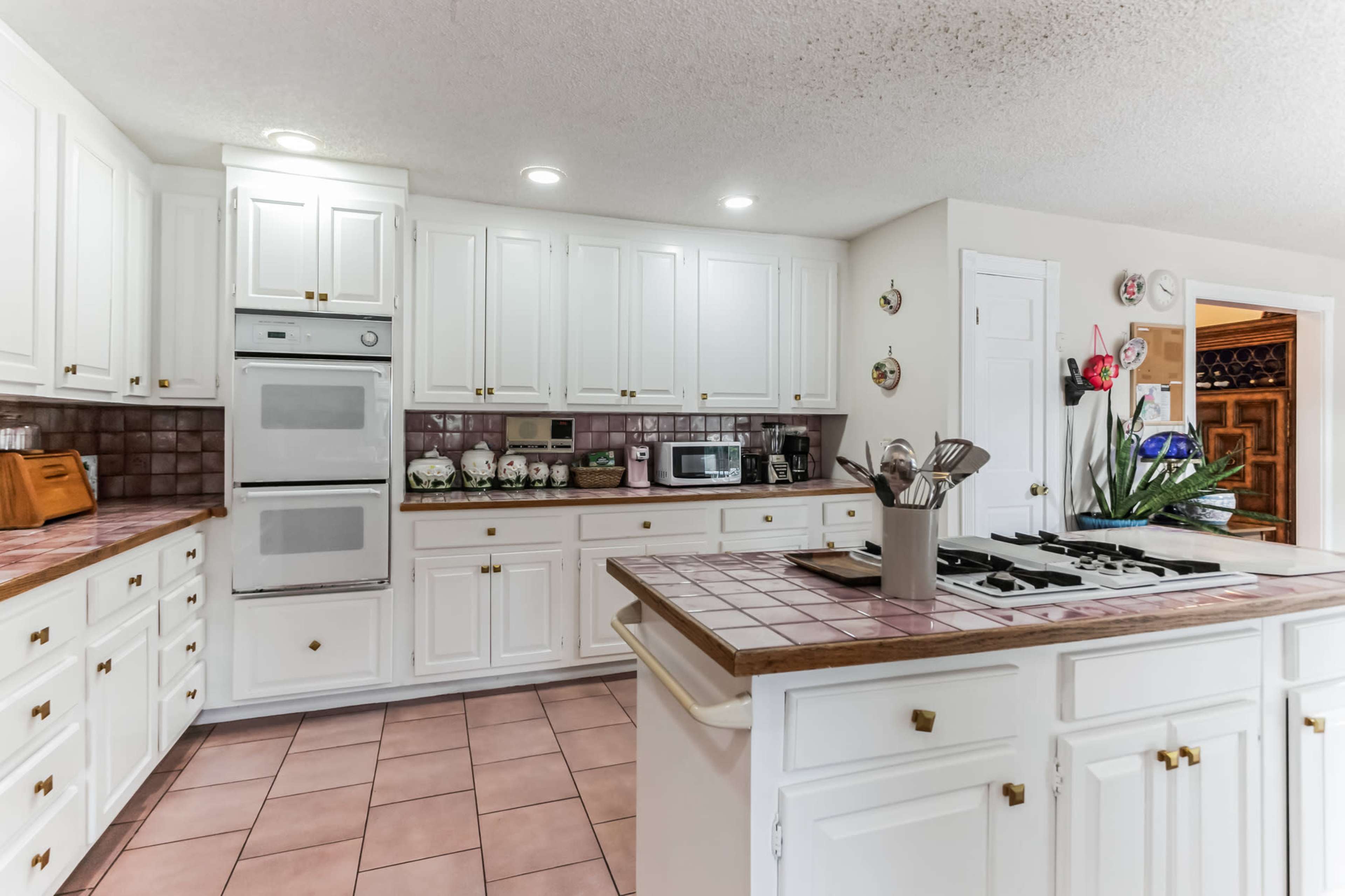 A spacious kitchen featuring white cabinetry, a central island with a stovetop, and tiled countertops.
