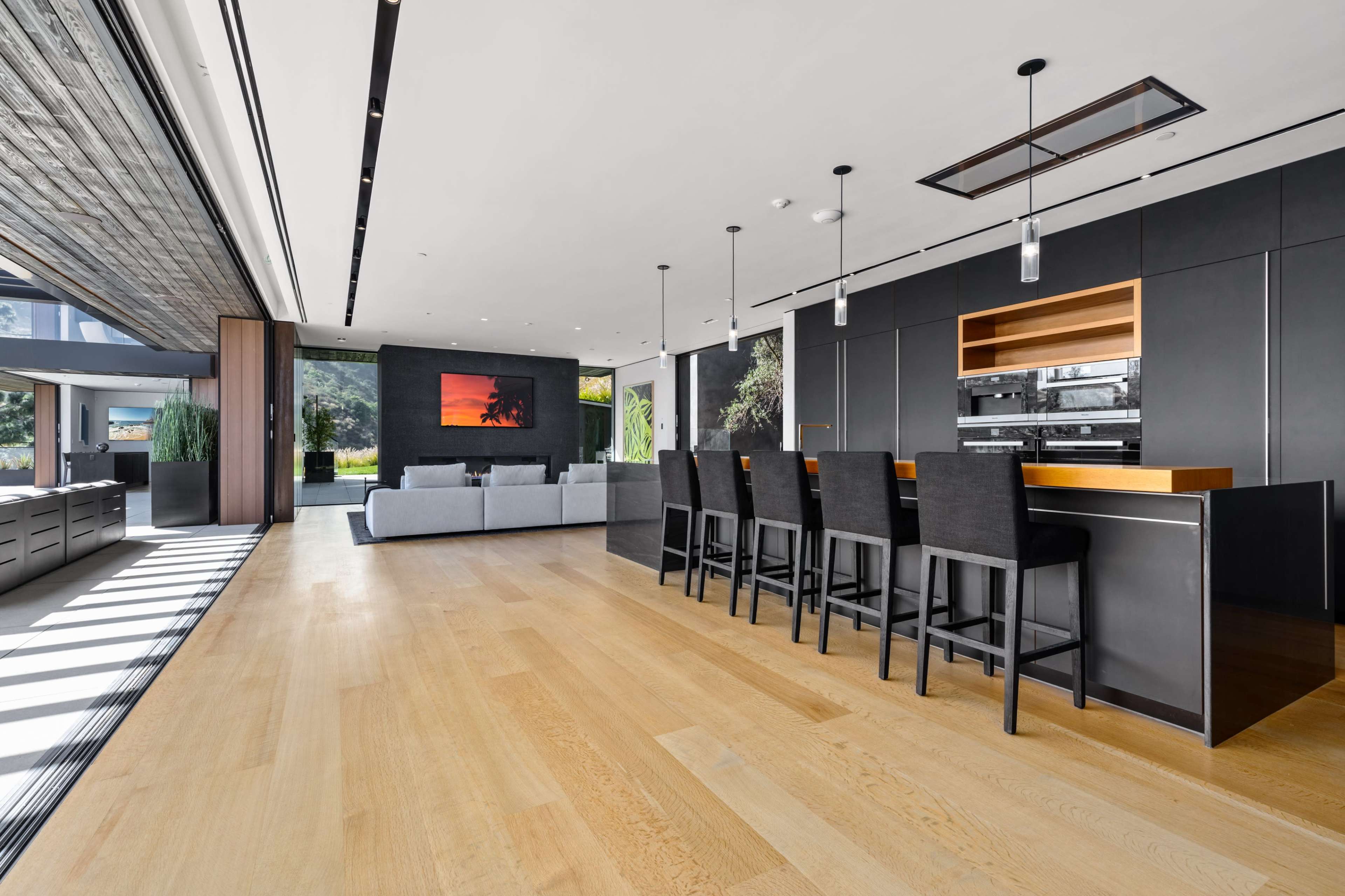 The image shows a modern, open-concept living space featuring a kitchen with bar seating, a living area with a large sofa, and a wall-mounted artwork.