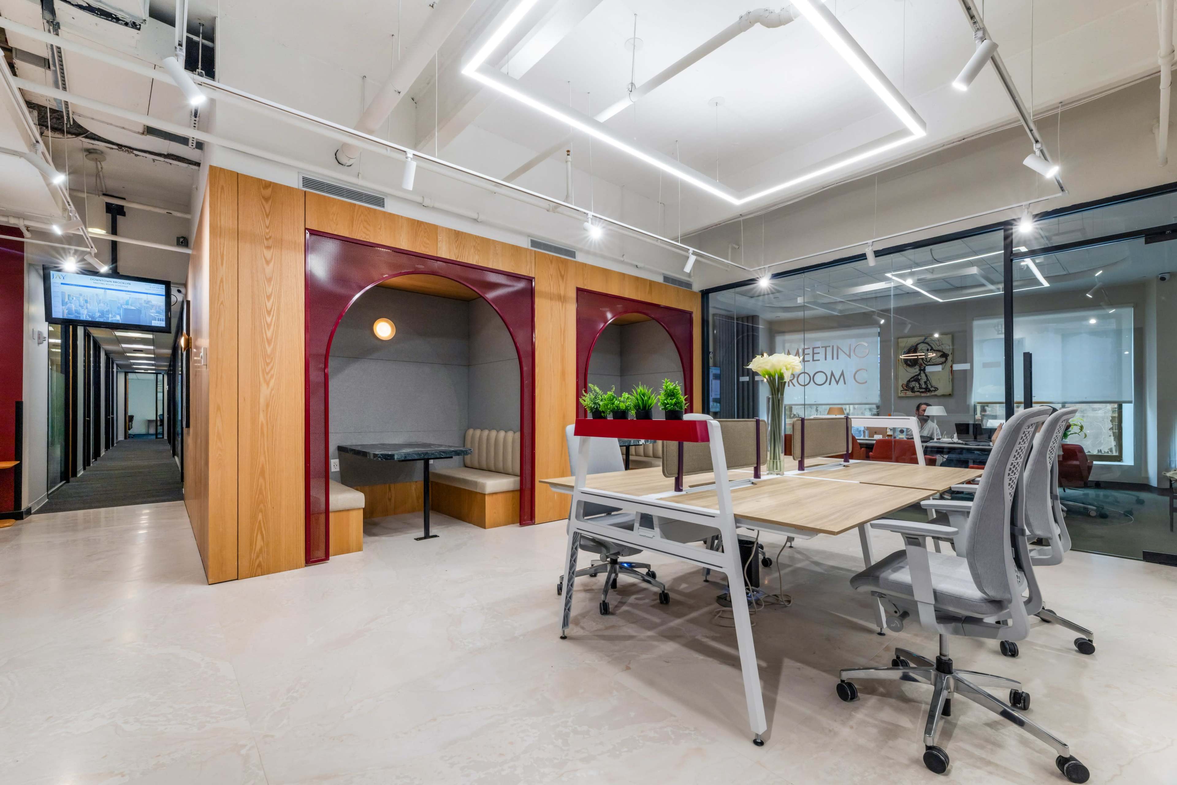 The image depicts a modern office space featuring a meeting area with a table and chairs, bordered by wooden archways and soundproof booths.