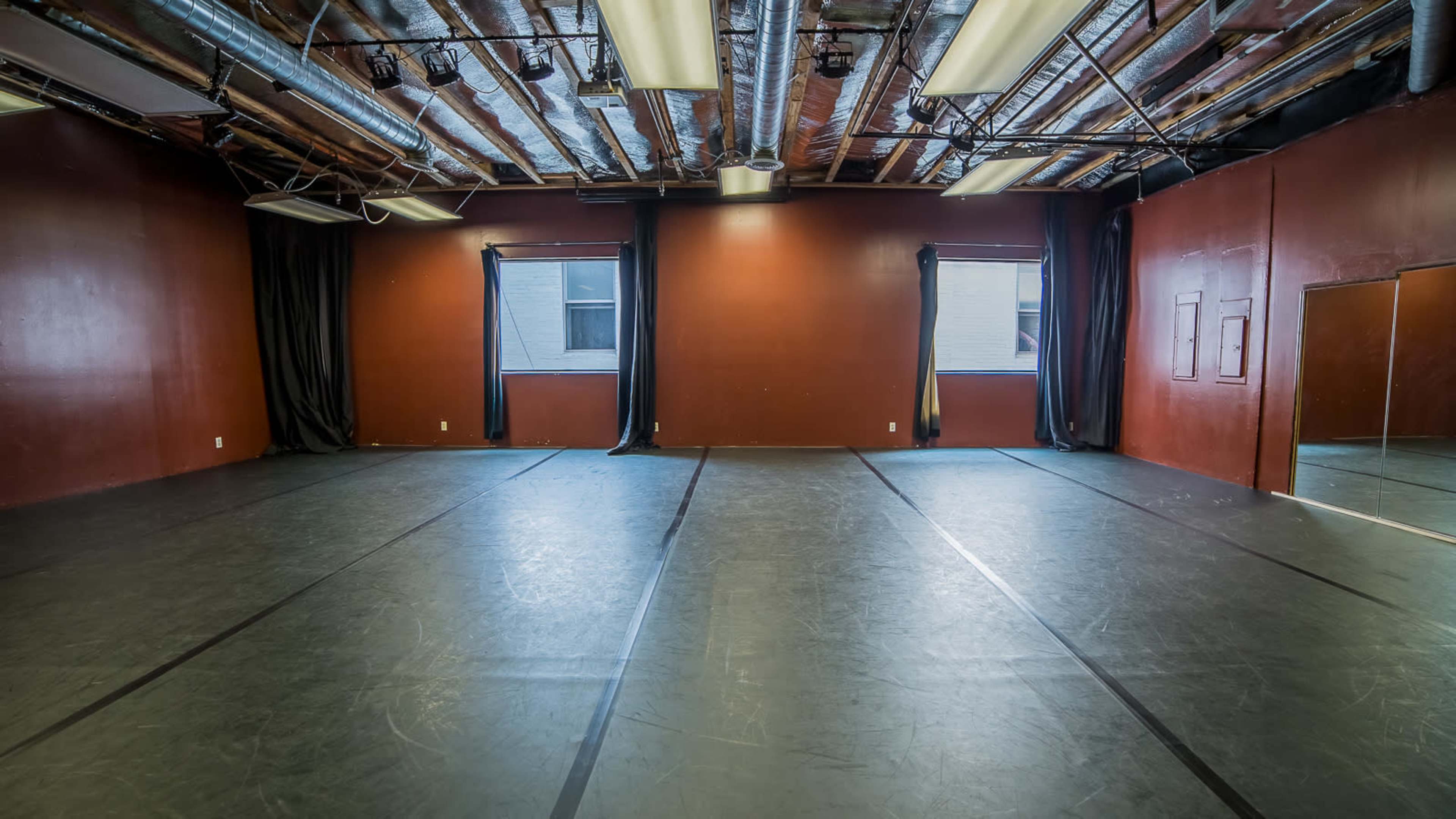 The image shows an empty dance studio with dark walls, wooden beams on the ceiling, and a large mirrored wall.