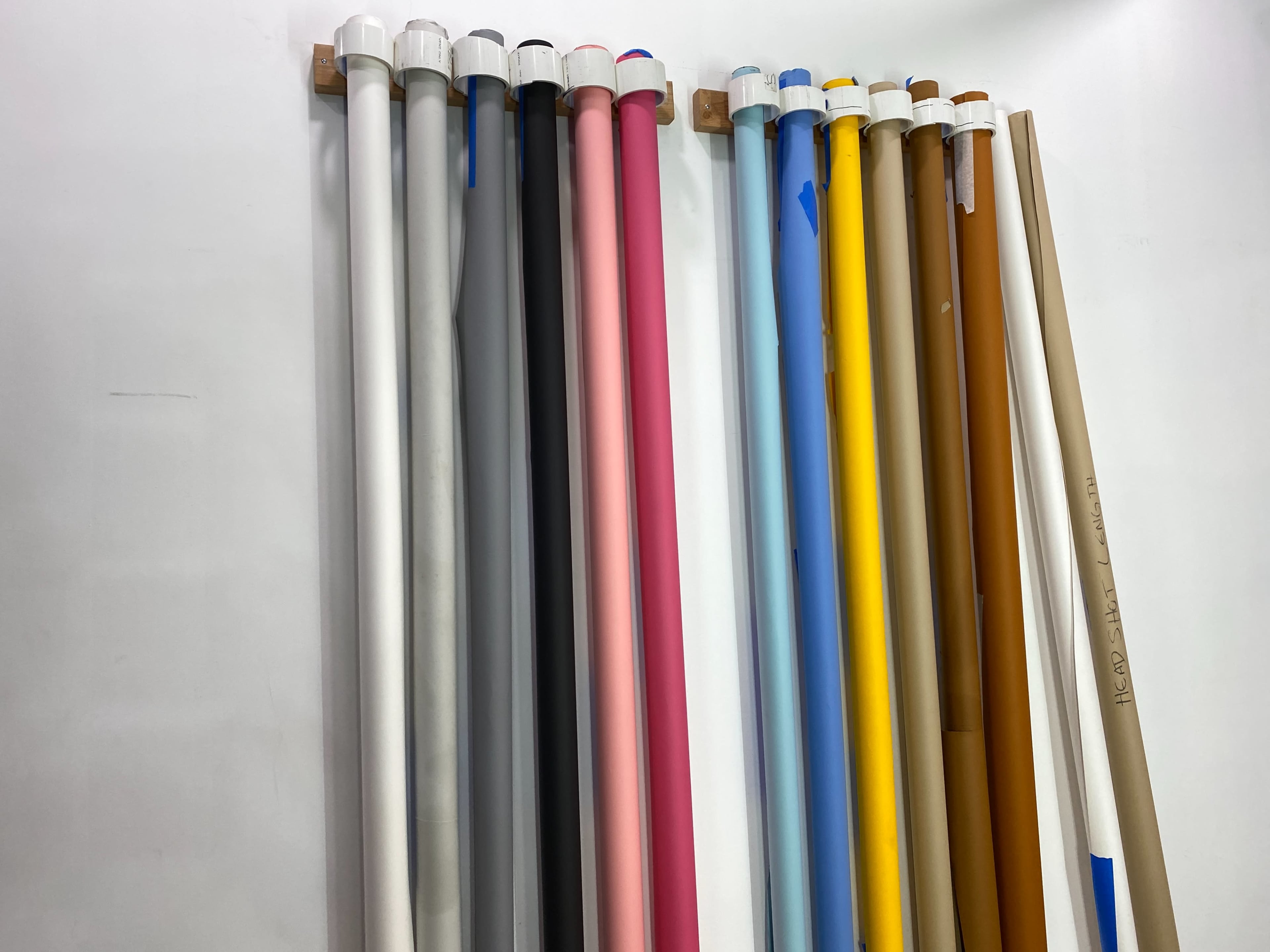 The image shows a collection of vertical rolls of colored paper or backdrop material arranged against a white wall.