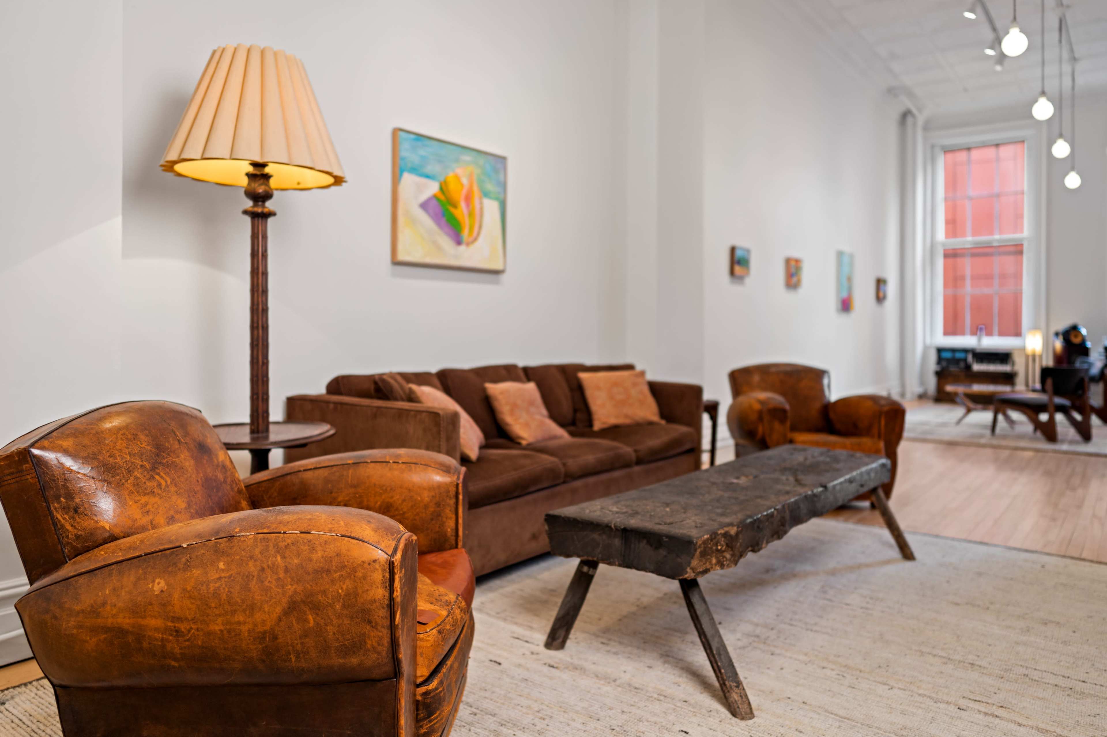 A spacious living area featuring a brown sofa, two leather armchairs, and a wooden coffee table, with artwork displayed on the walls.