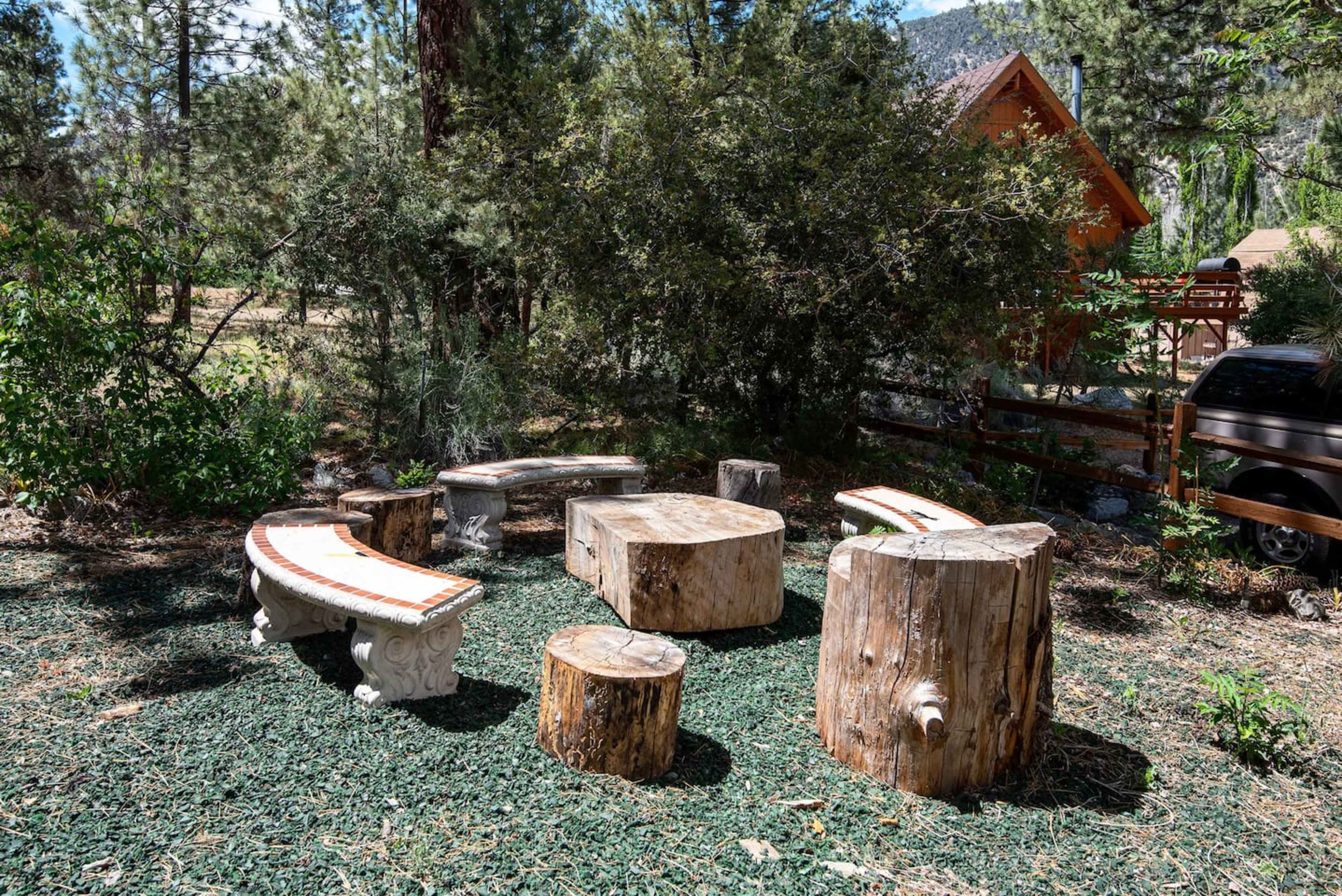 A rustic outdoor seating area made of sliced logs and stone benches, surrounded by greenery.