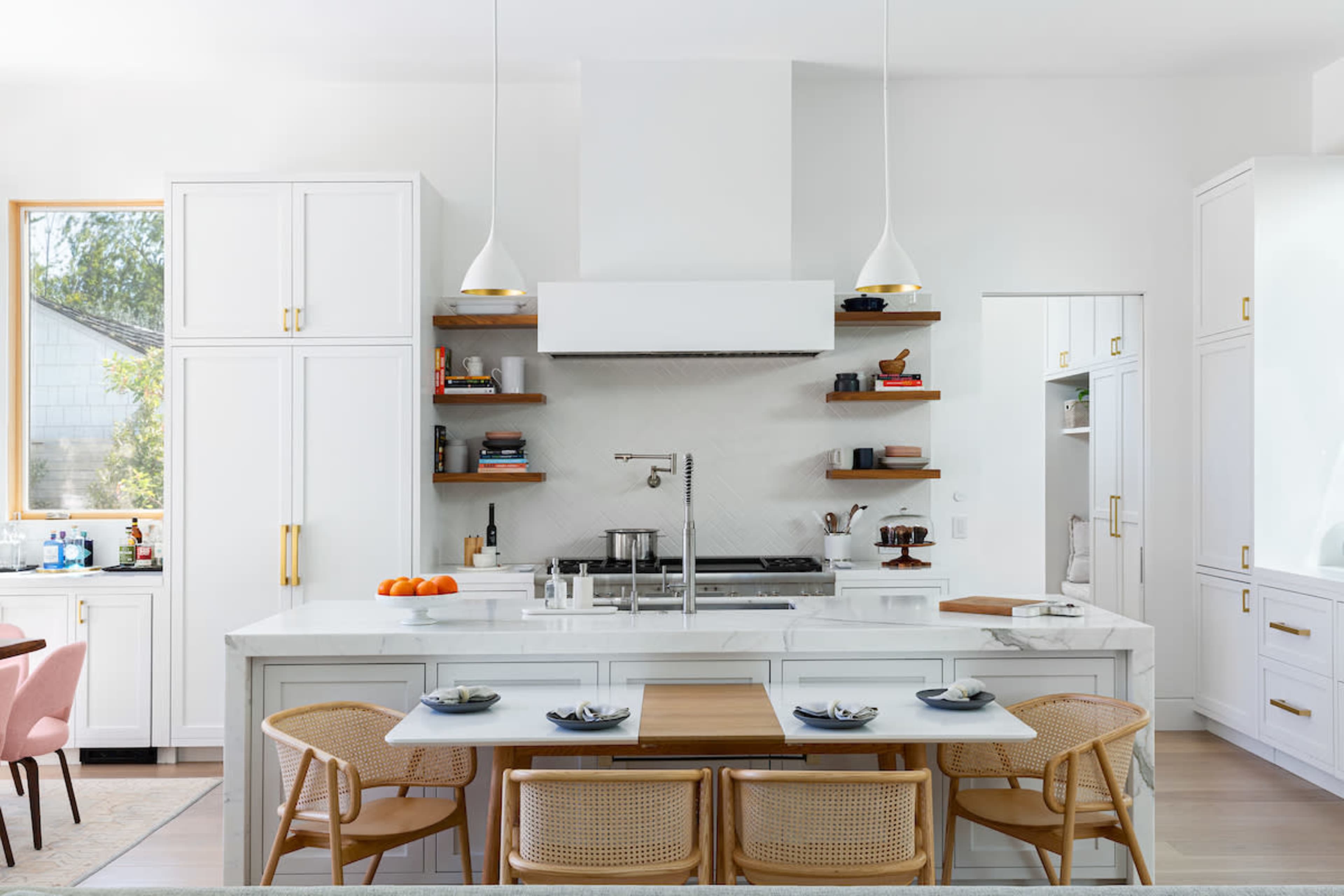 A modern kitchen features white cabinetry, a central island with a wooden tabletop, and open shelving displaying kitchenware.