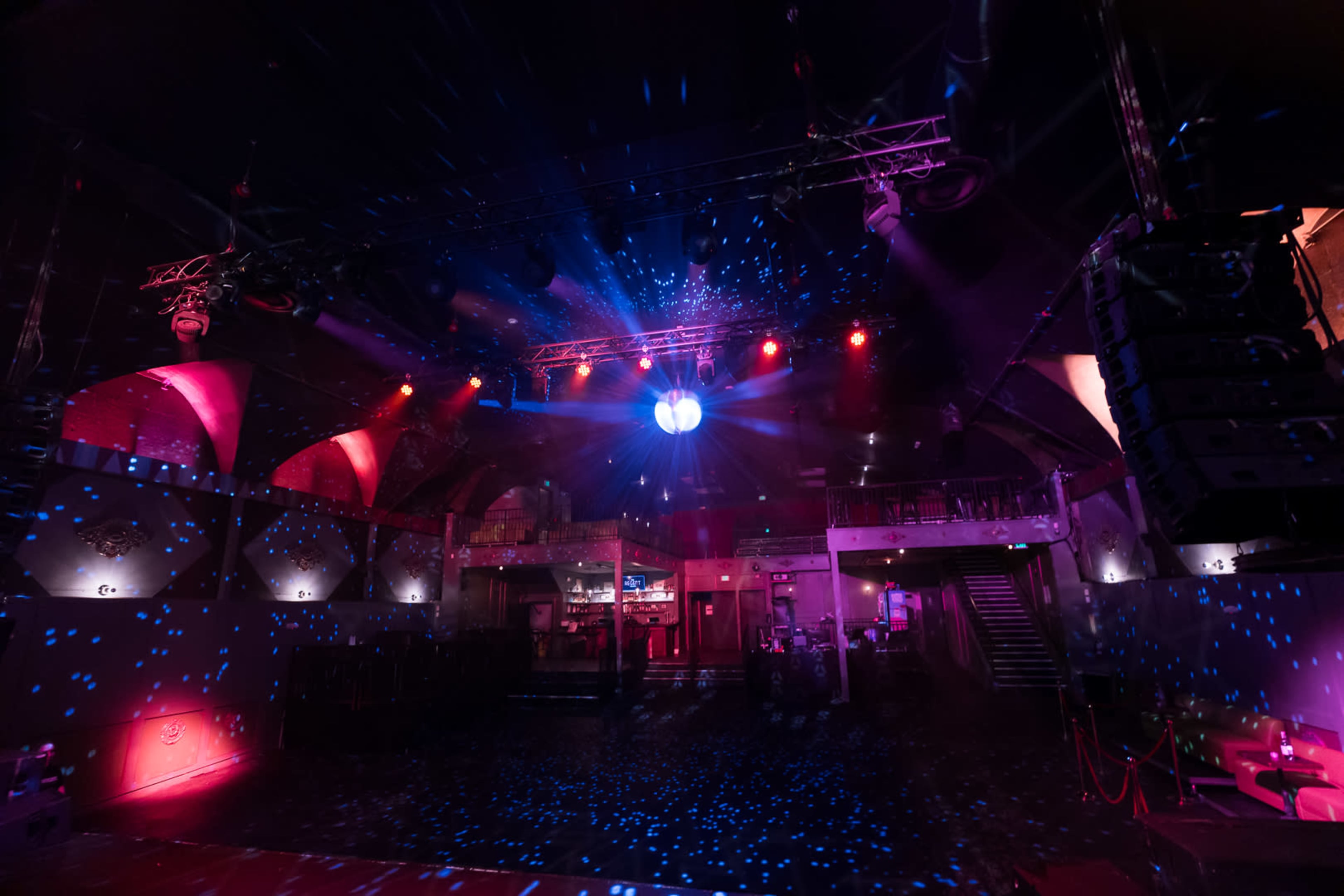The image shows an empty nightclub with colorful lights and a disco ball reflecting patterns on the dance floor.