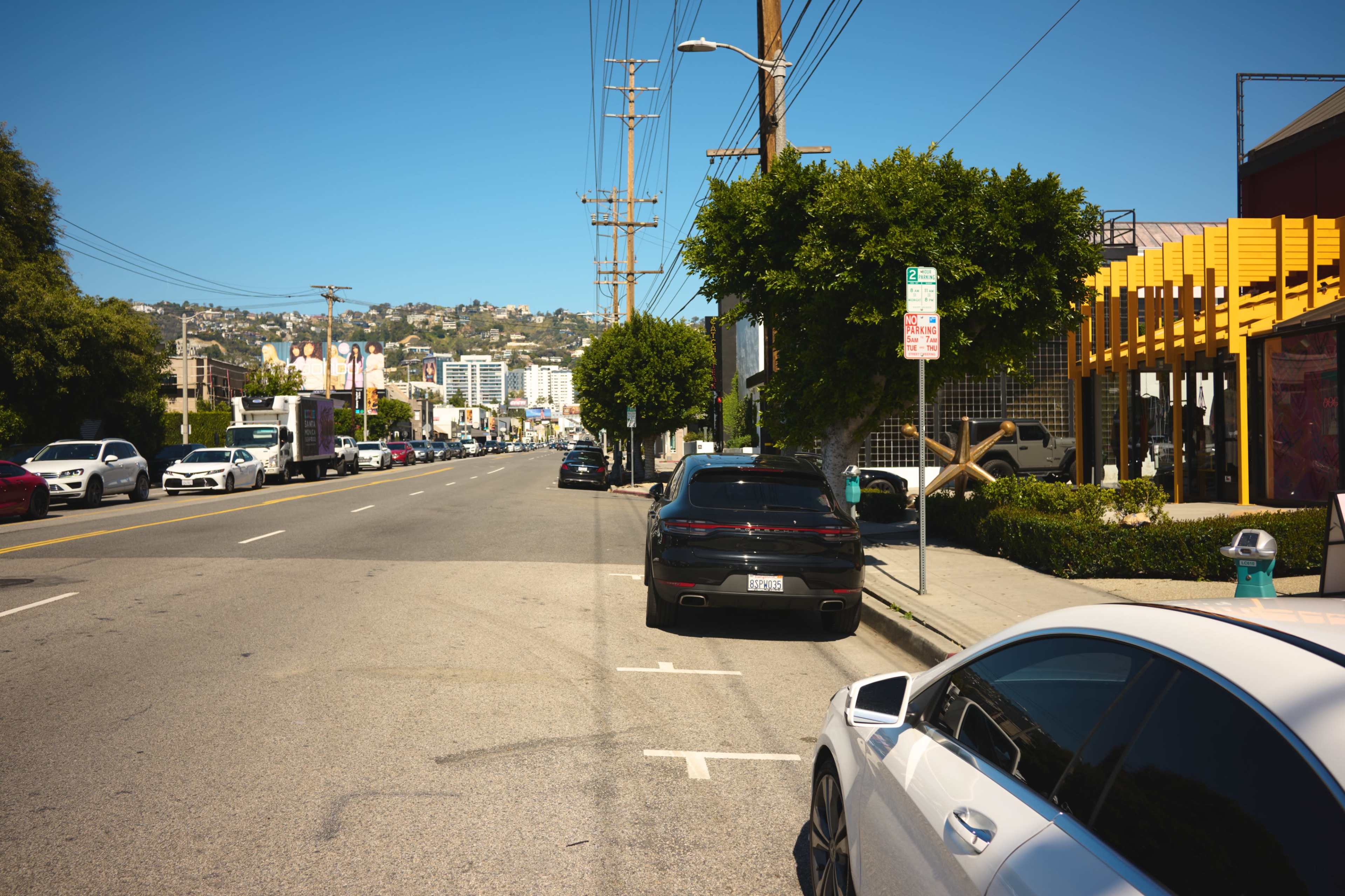 A sunny street lined with parked cars, telephone poles, and buildings in the background on a clear day.