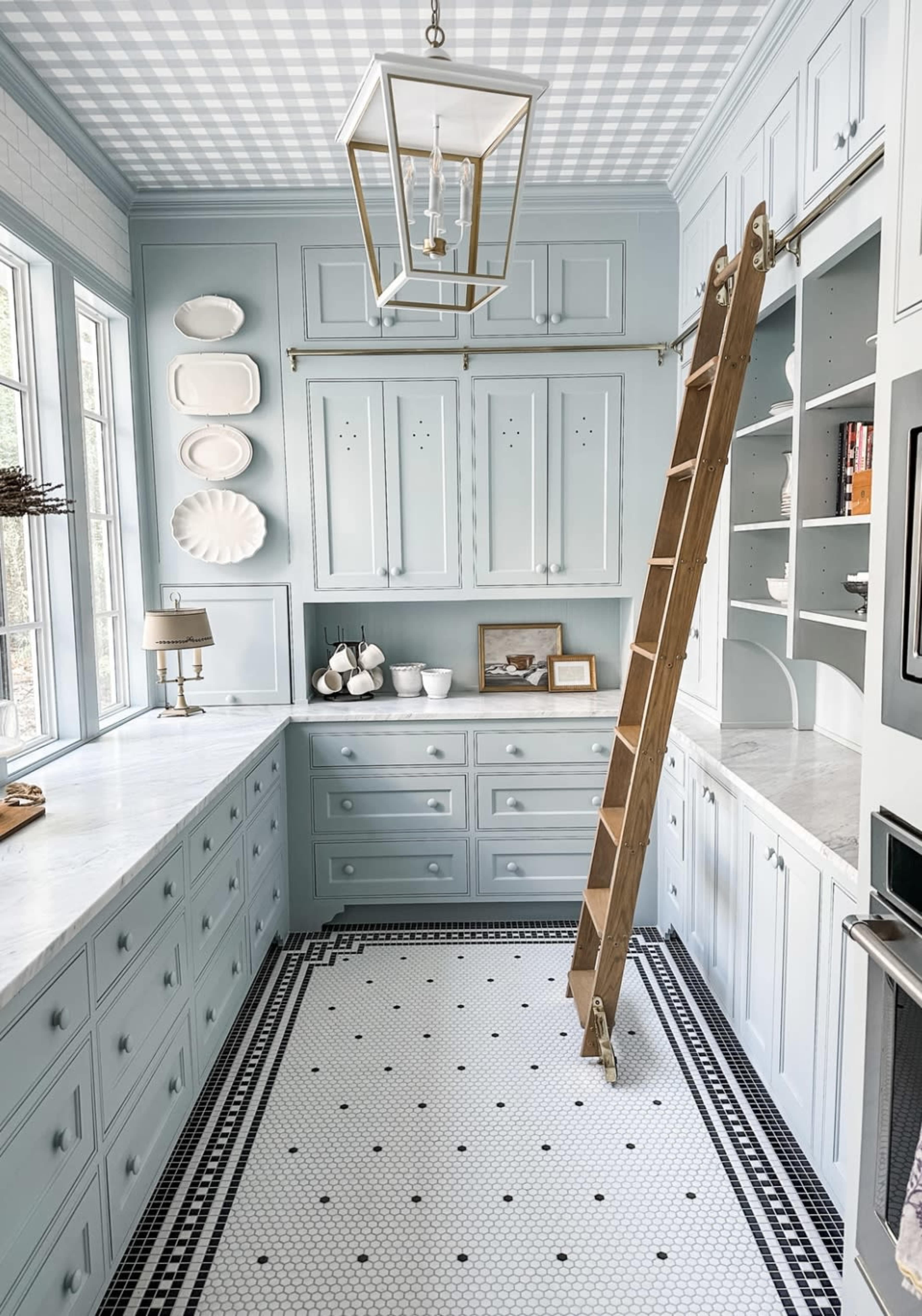 A light blue kitchen features cabinetry, a wooden ladder against the wall, and a checkered ceiling accompanied by white and black tiled flooring.