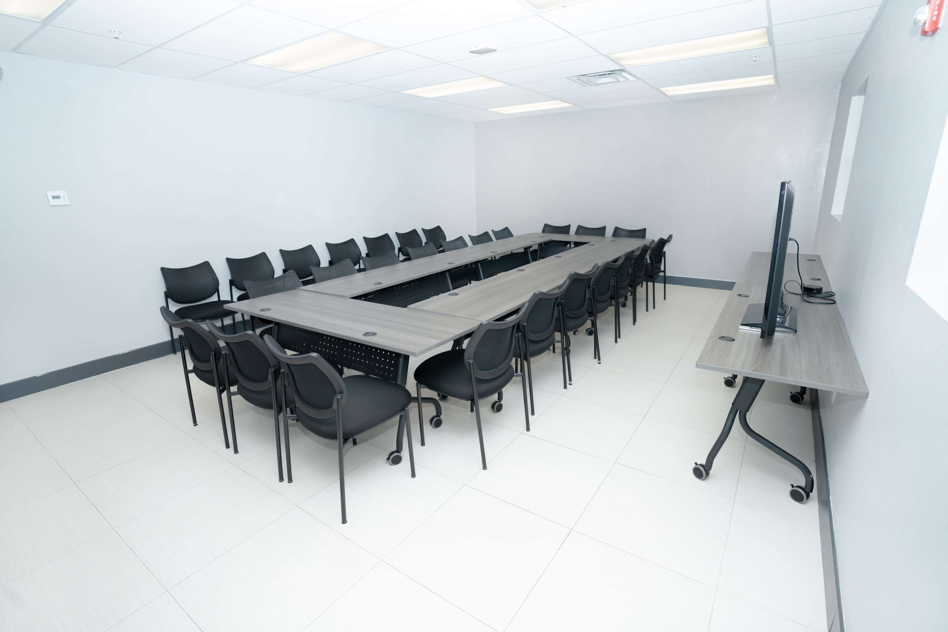 A large conference room with a rectangular table surrounded by multiple black chairs and a television mounted on the wall.