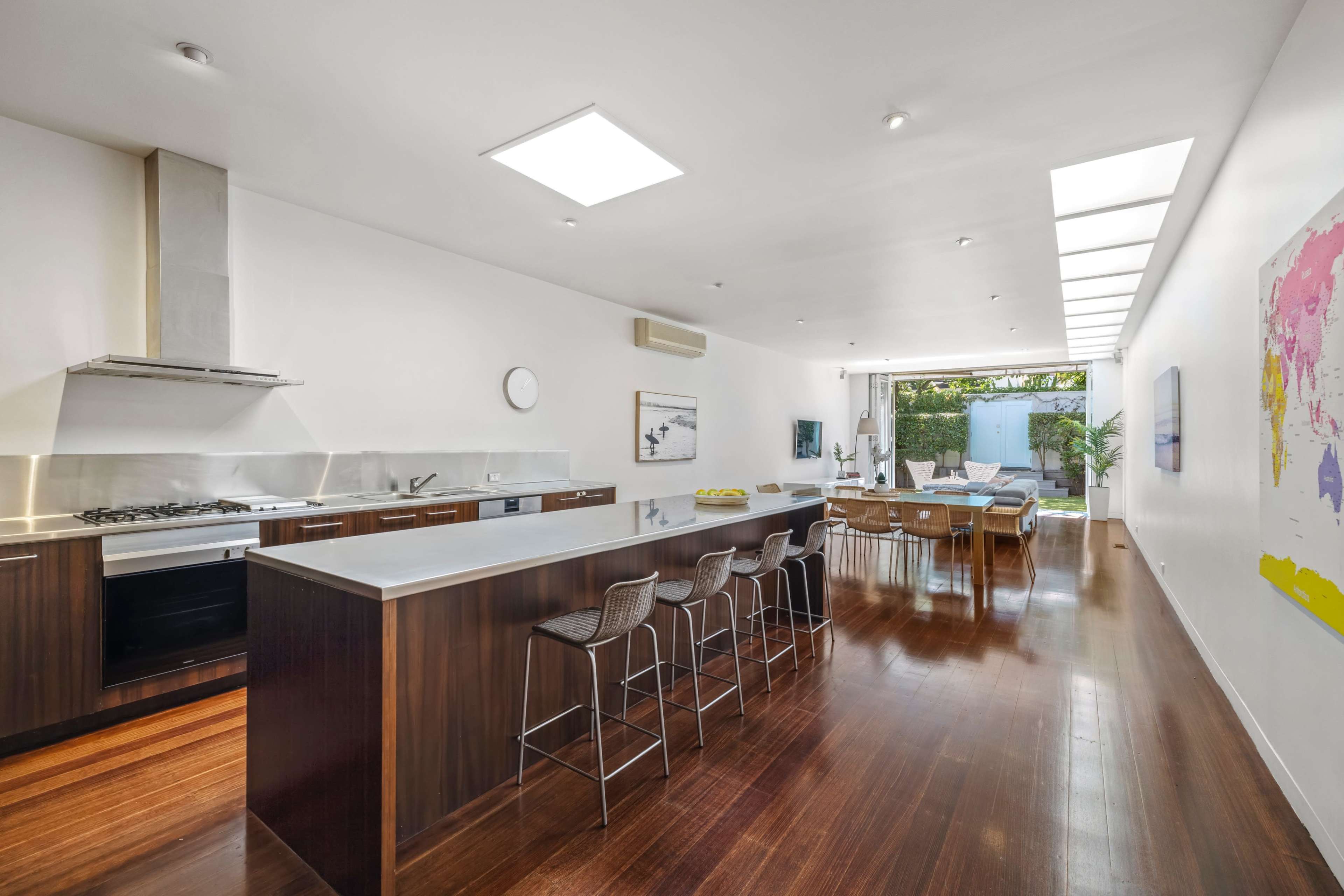 A modern kitchen with a long island bar and a dining area, featuring large windows that allow natural light to flow in.