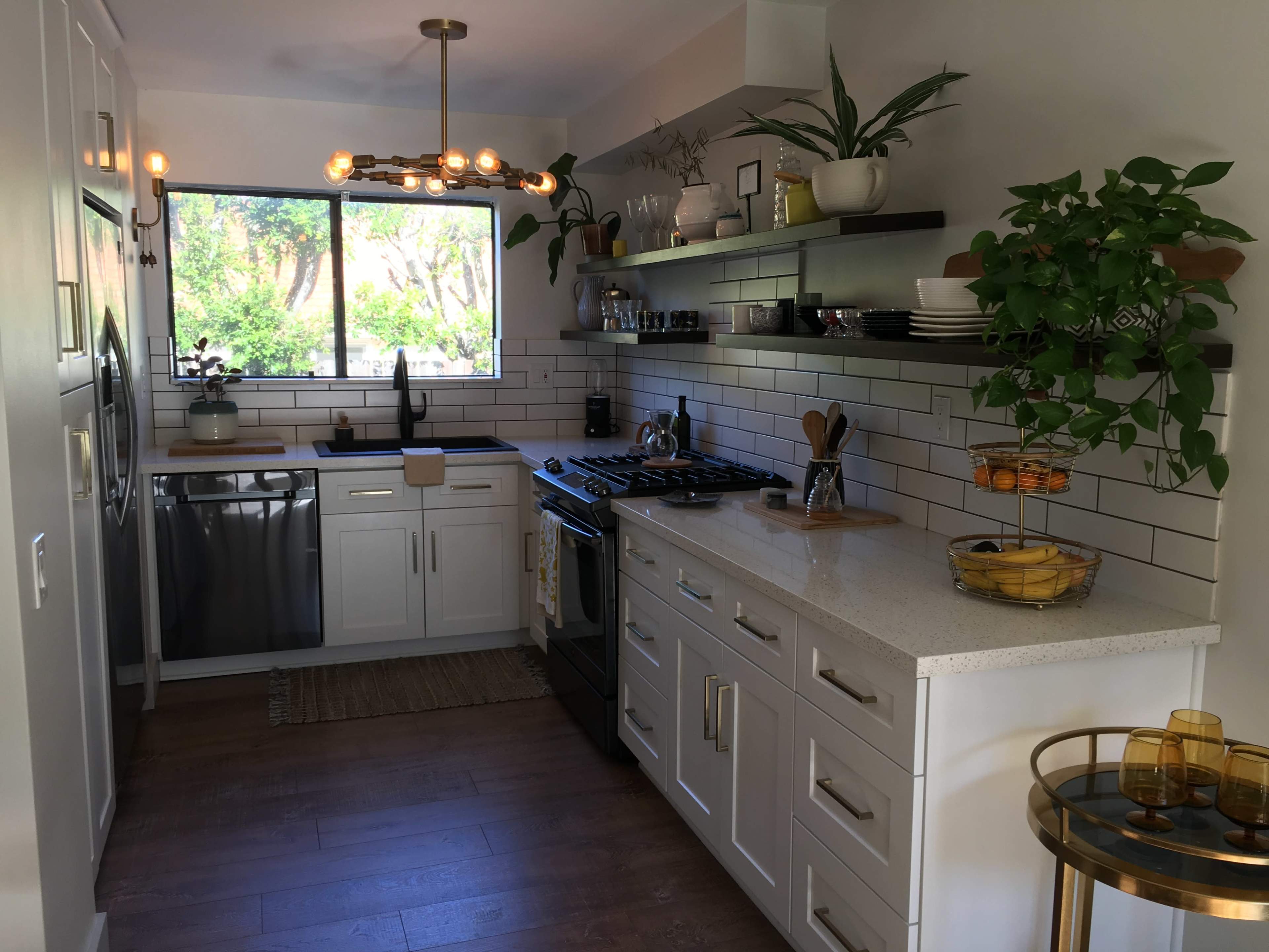 A modern kitchen features stainless steel appliances, white cabinetry, a quartz countertop, and an ample window overlooking greenery.