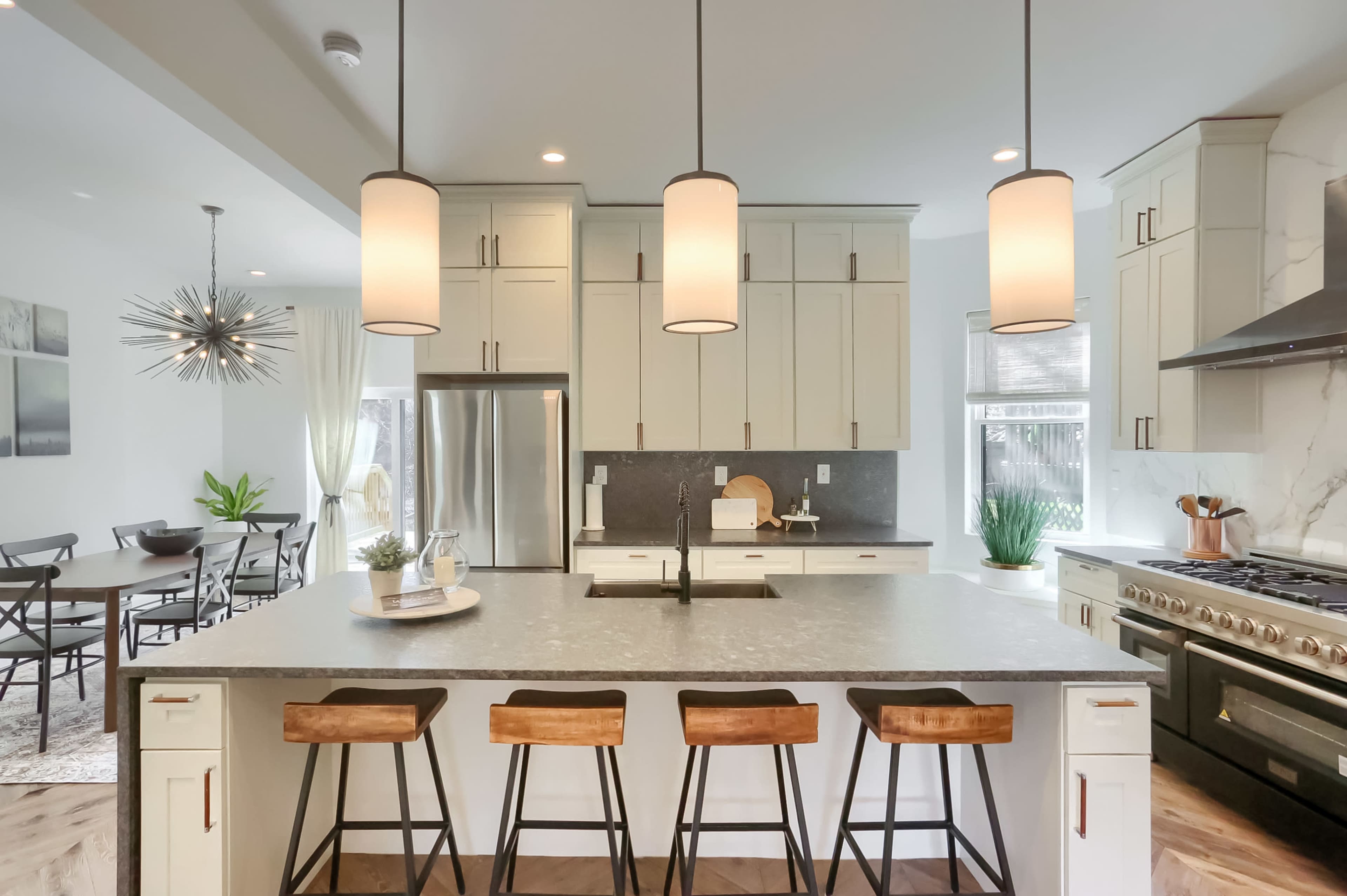 A modern kitchen features a large island with seating, pendant lights, and stainless steel appliances set against light-colored cabinetry.
