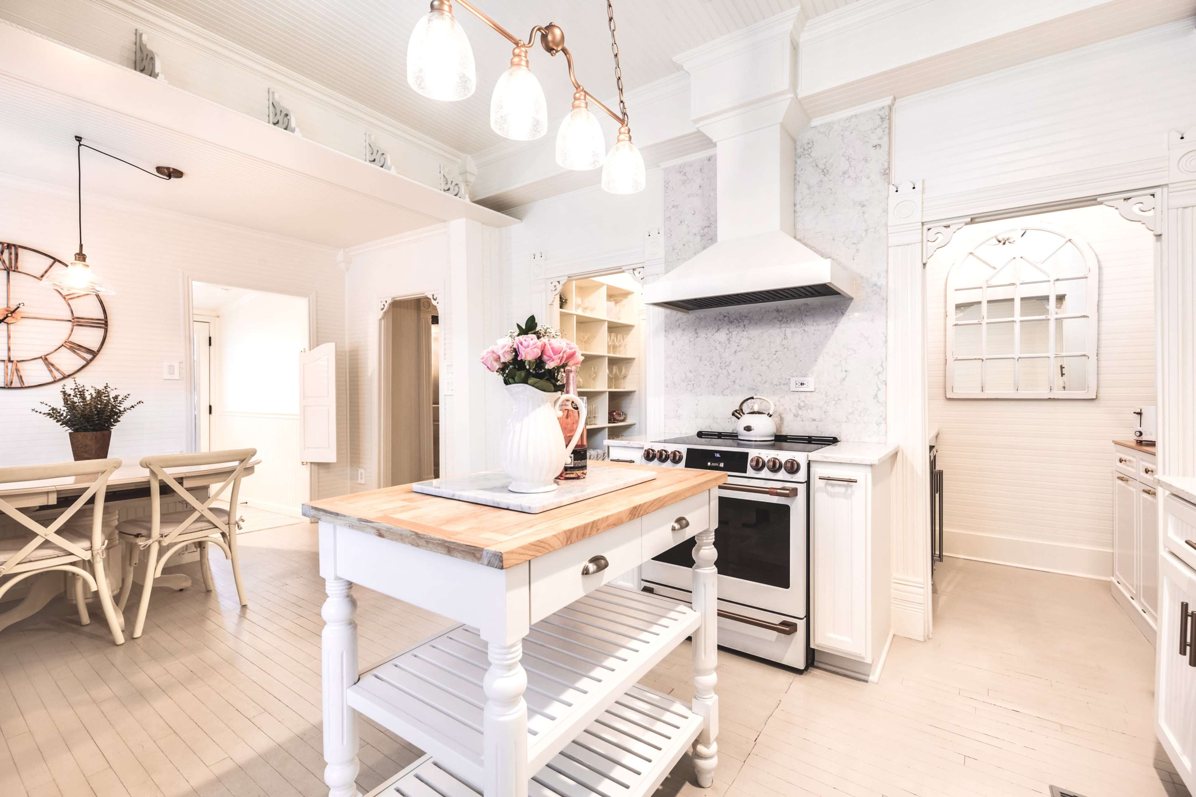 The image shows a bright and modern kitchen featuring white cabinetry, a central island with a wooden top, and a stove beneath a vent hood.