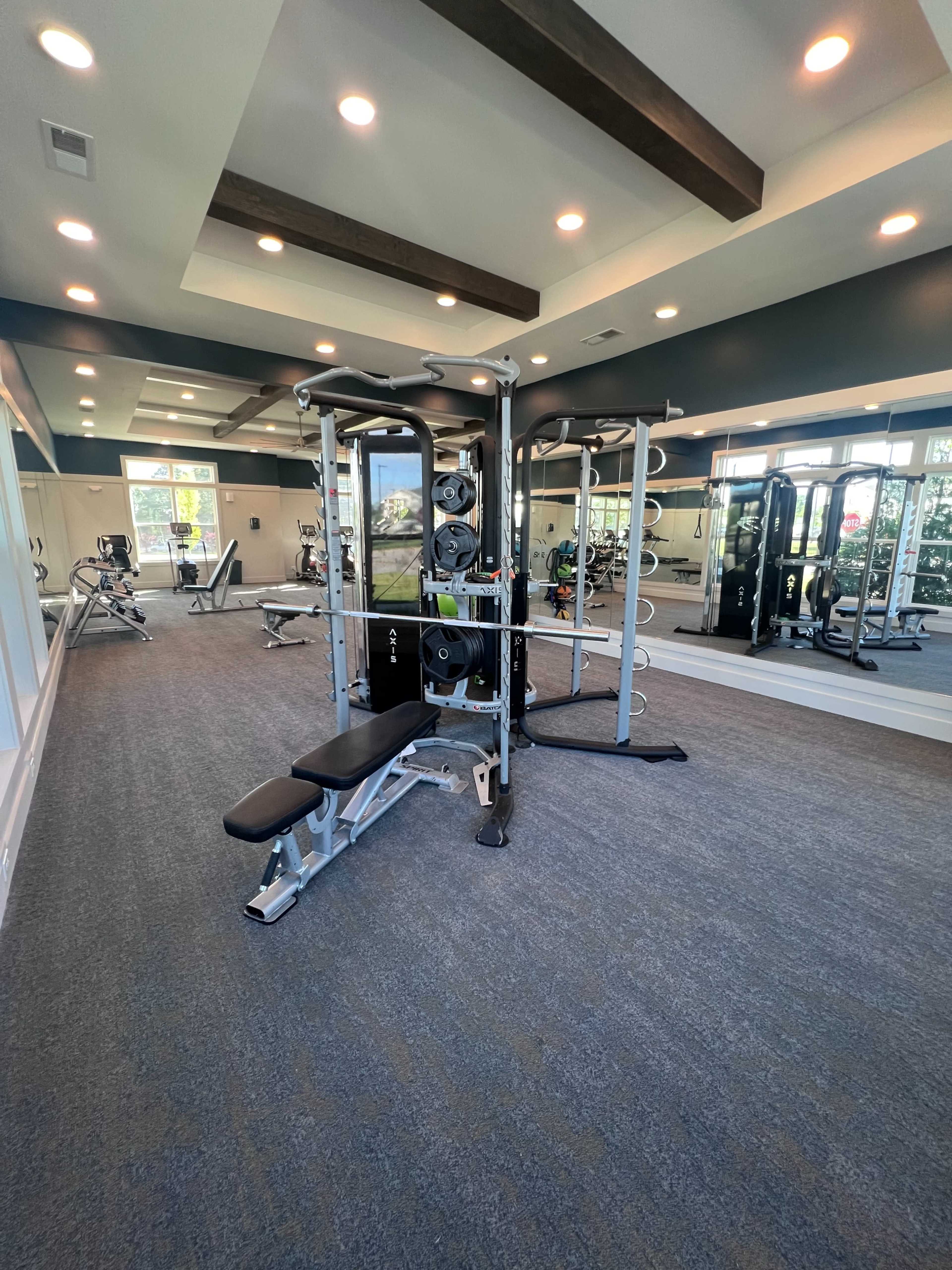 The image shows a modern gym interior featuring weightlifting equipment and mirrors, illuminated by overhead lights.