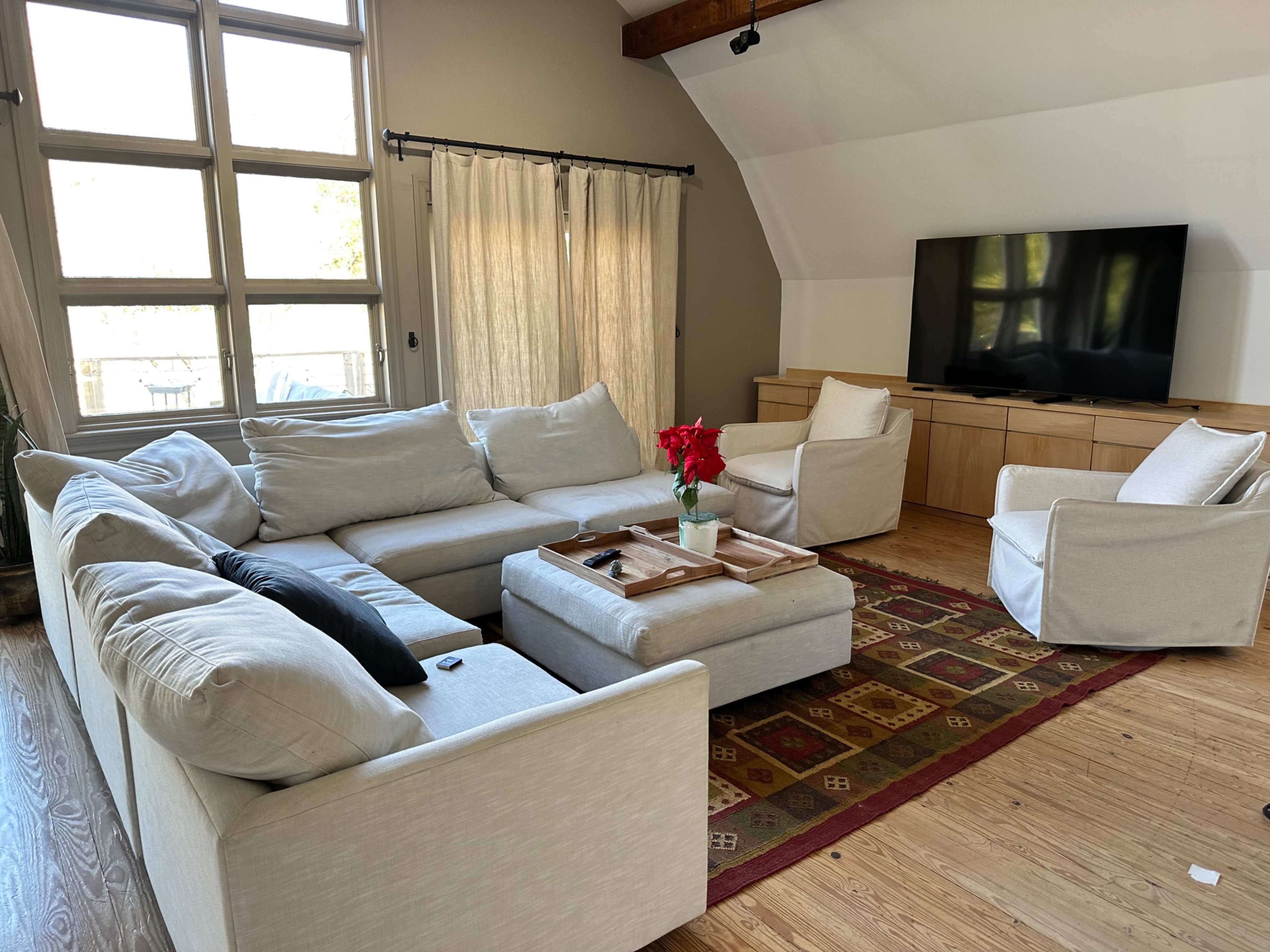 A spacious living room with a large sectional sofa, a wooden media console, a television, and a central coffee table with flowers.