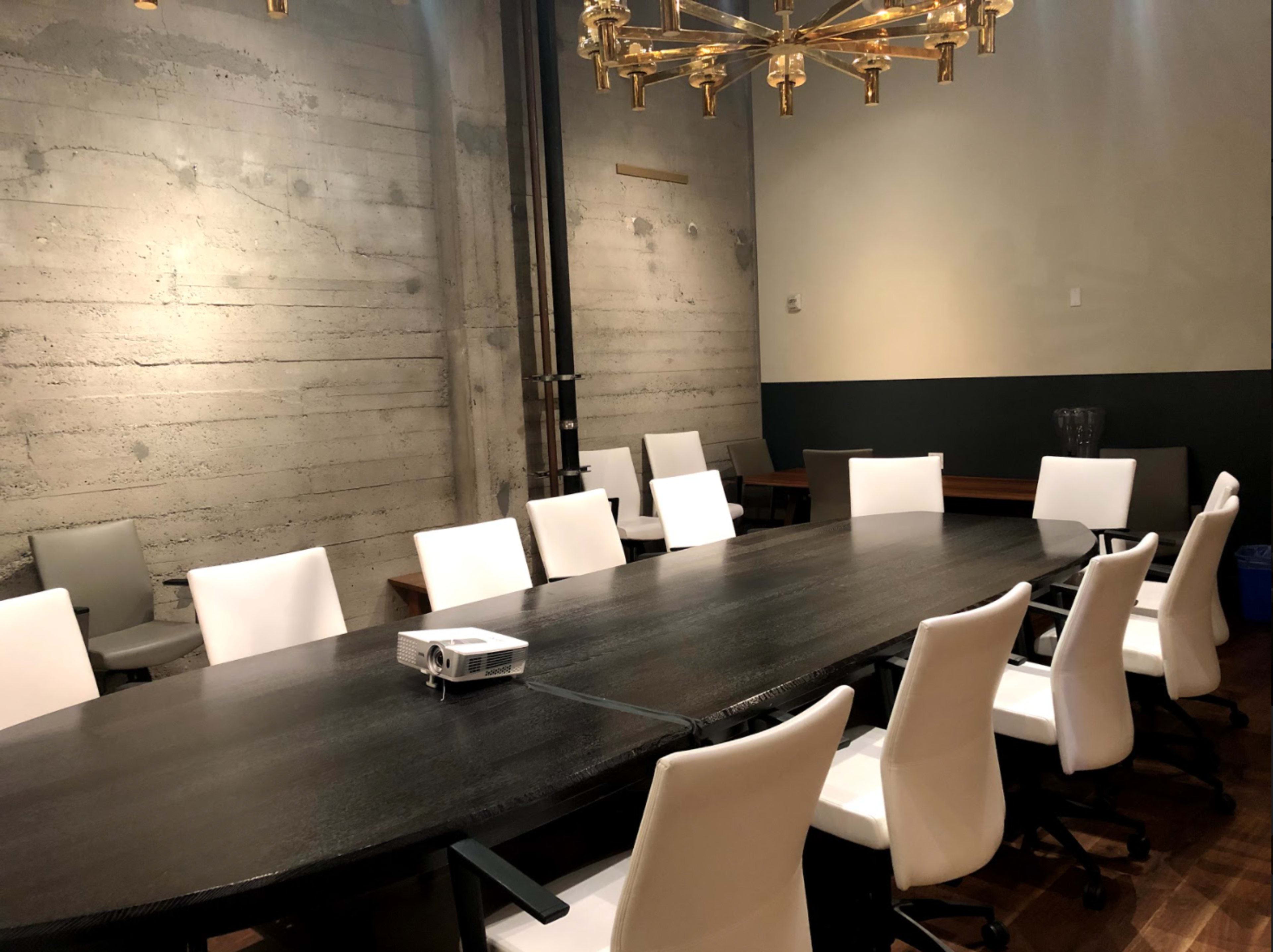 The room features a large, dark wooden conference table surrounded by white swivel chairs, with a projector placed at one end.