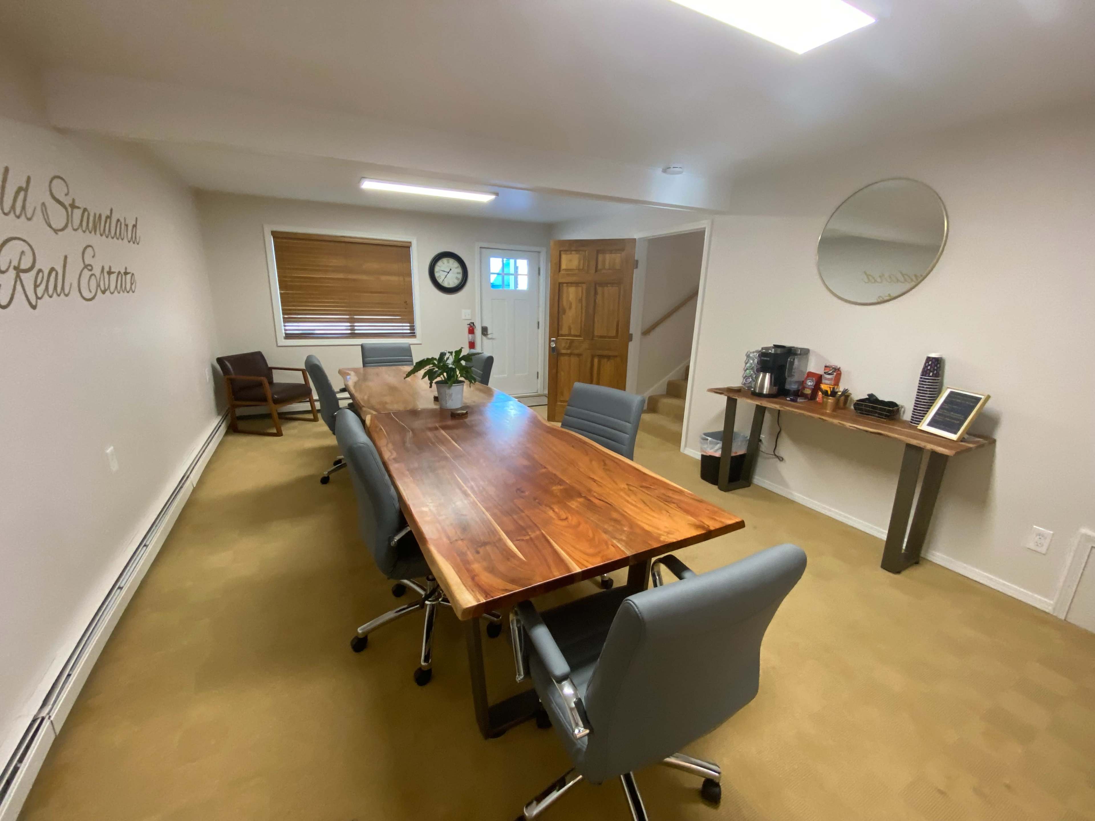 A spacious conference room with a large wooden table surrounded by gray chairs, and a coffee station in the corner.