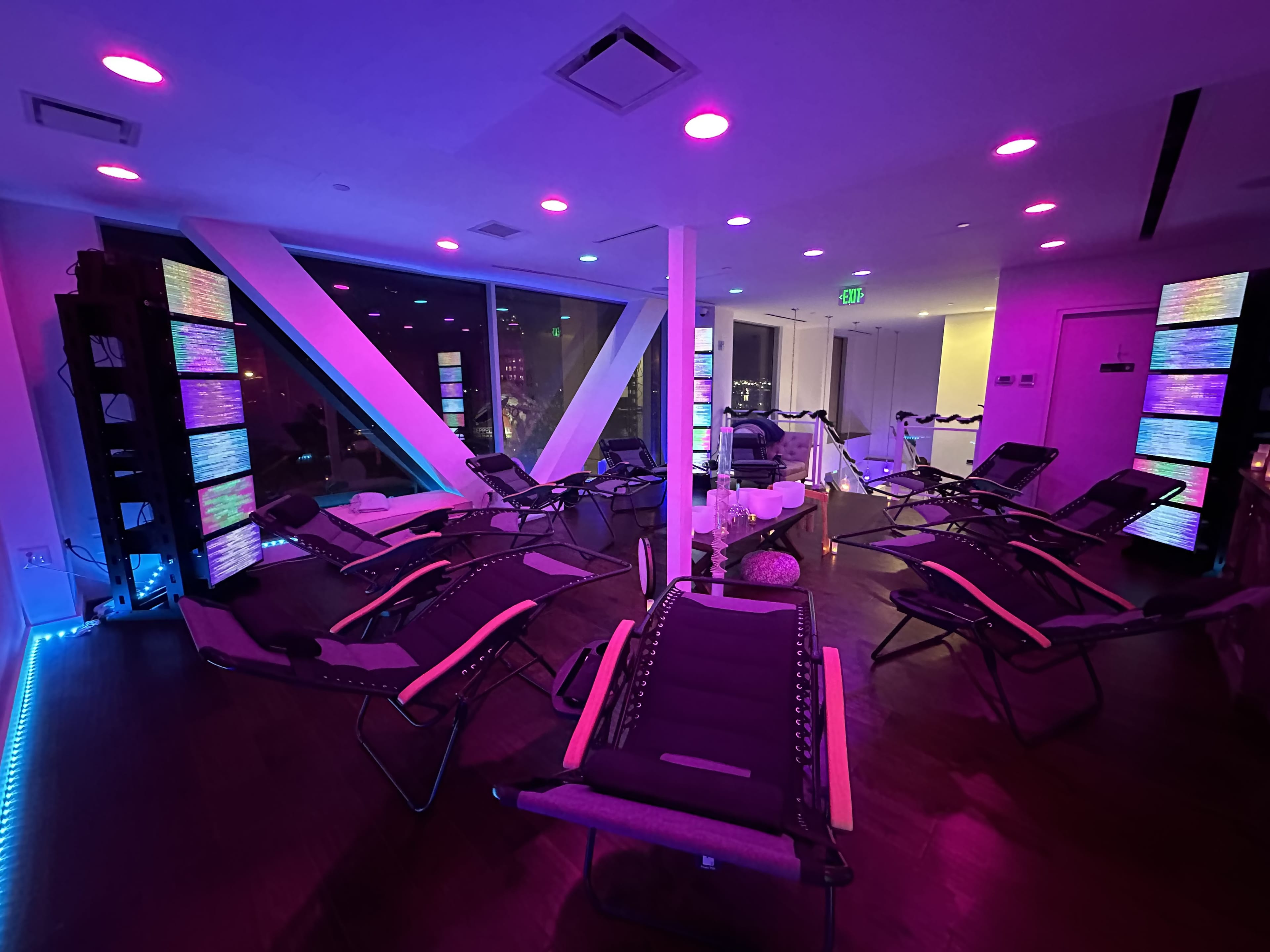 A dimly lit room features multiple reclining chairs arranged in a semi-circle, with colorful lights illuminating the walls and creating a relaxed atmosphere.