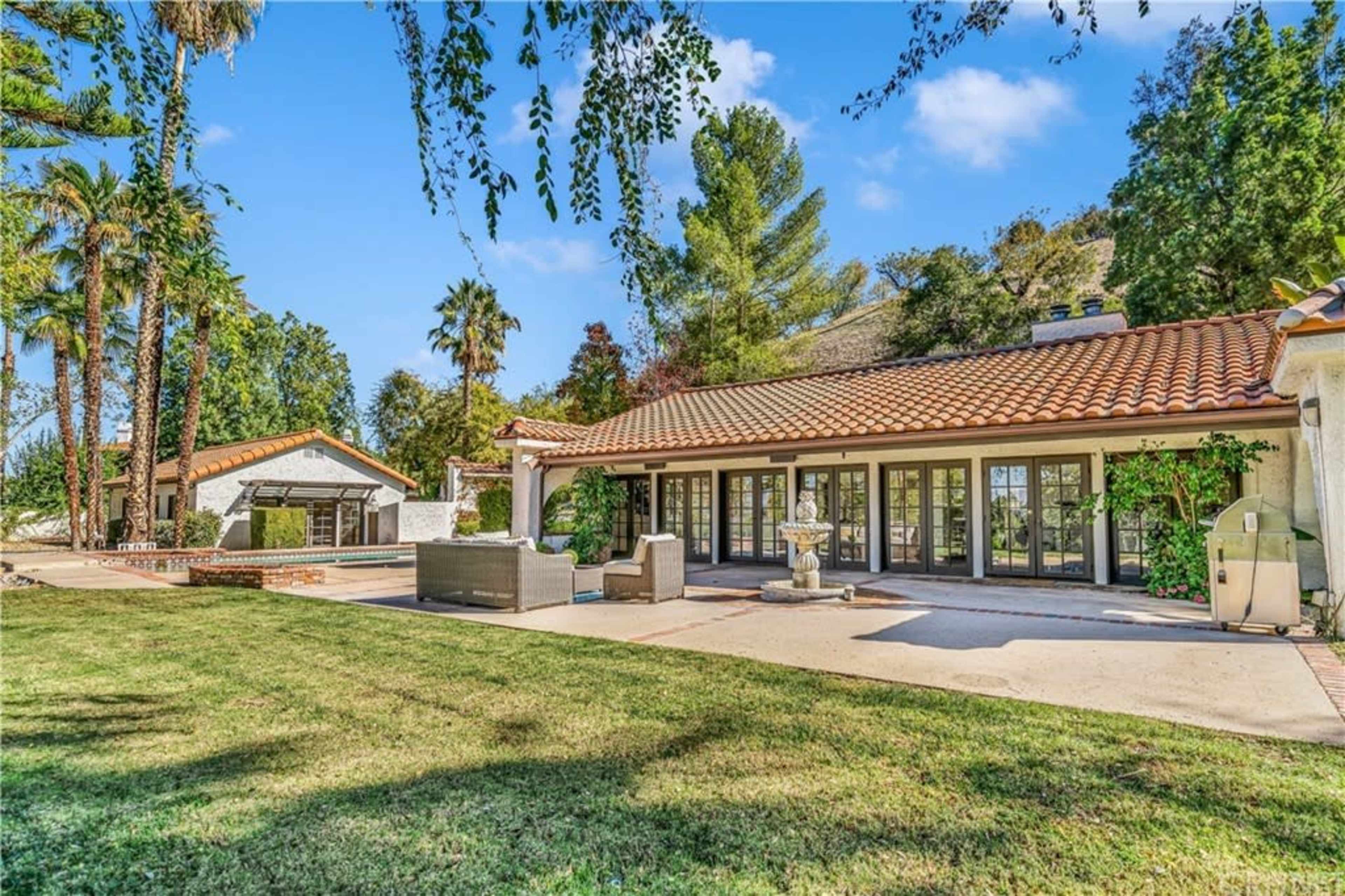A landscaped backyard with a brick patio, outdoor seating, and a house featuring a tiled roof and large glass doors.