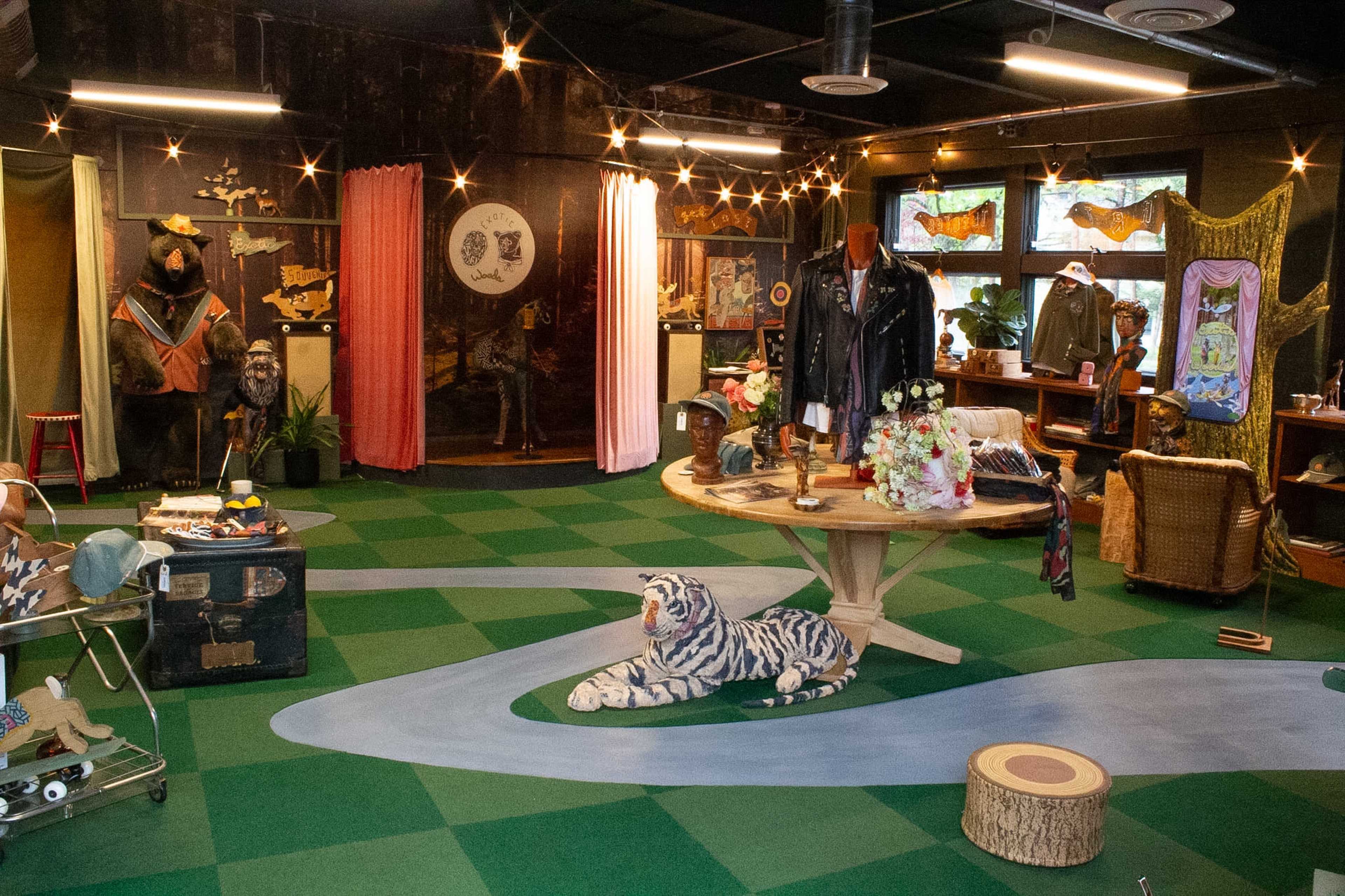 The scene features a whimsical boutique with animal-themed decor, showcasing clothing and accessories against a colorful backdrop, centered around a circular display table.