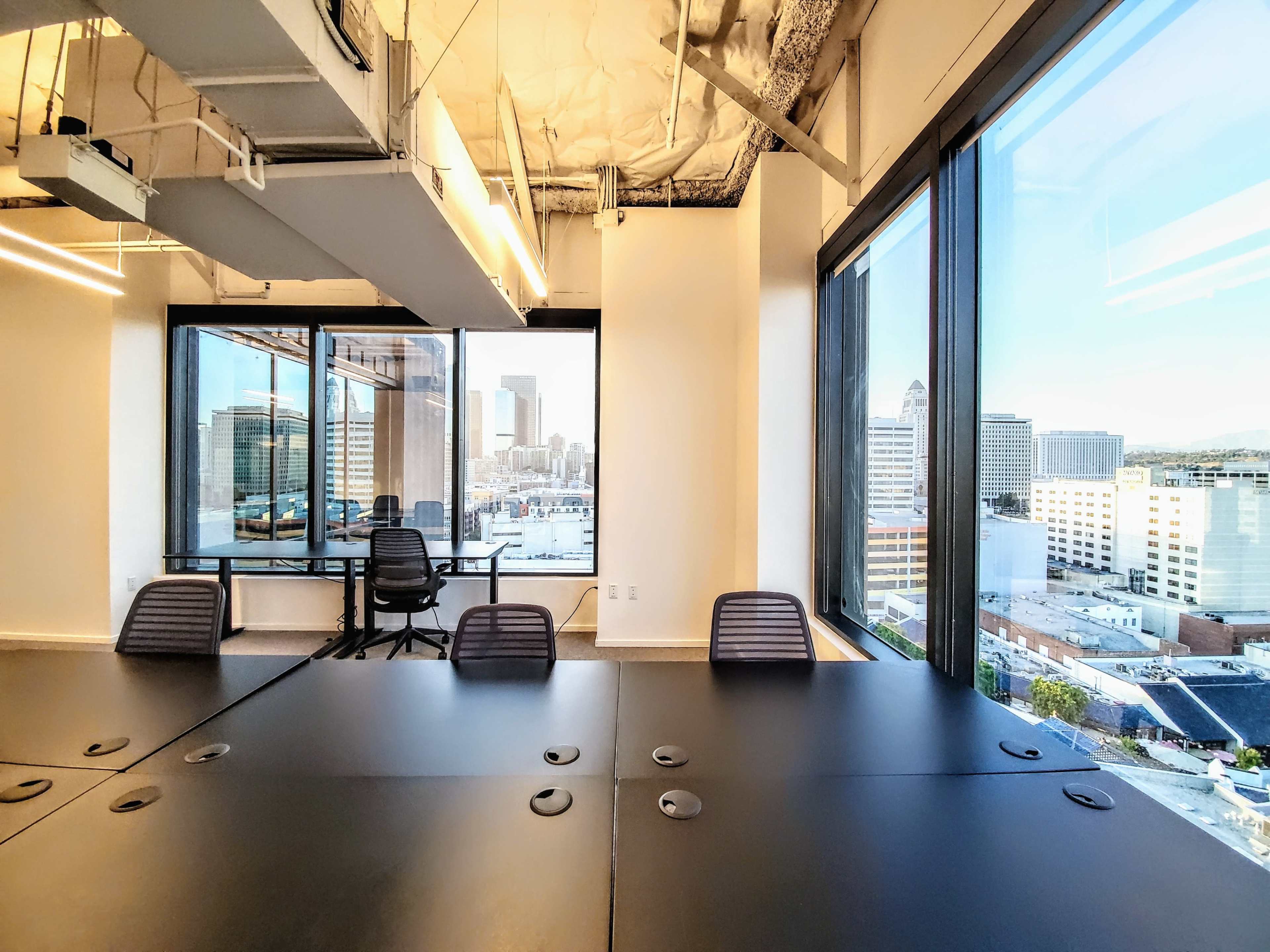 A conference room with a large black table and windows overlooking a city skyline.