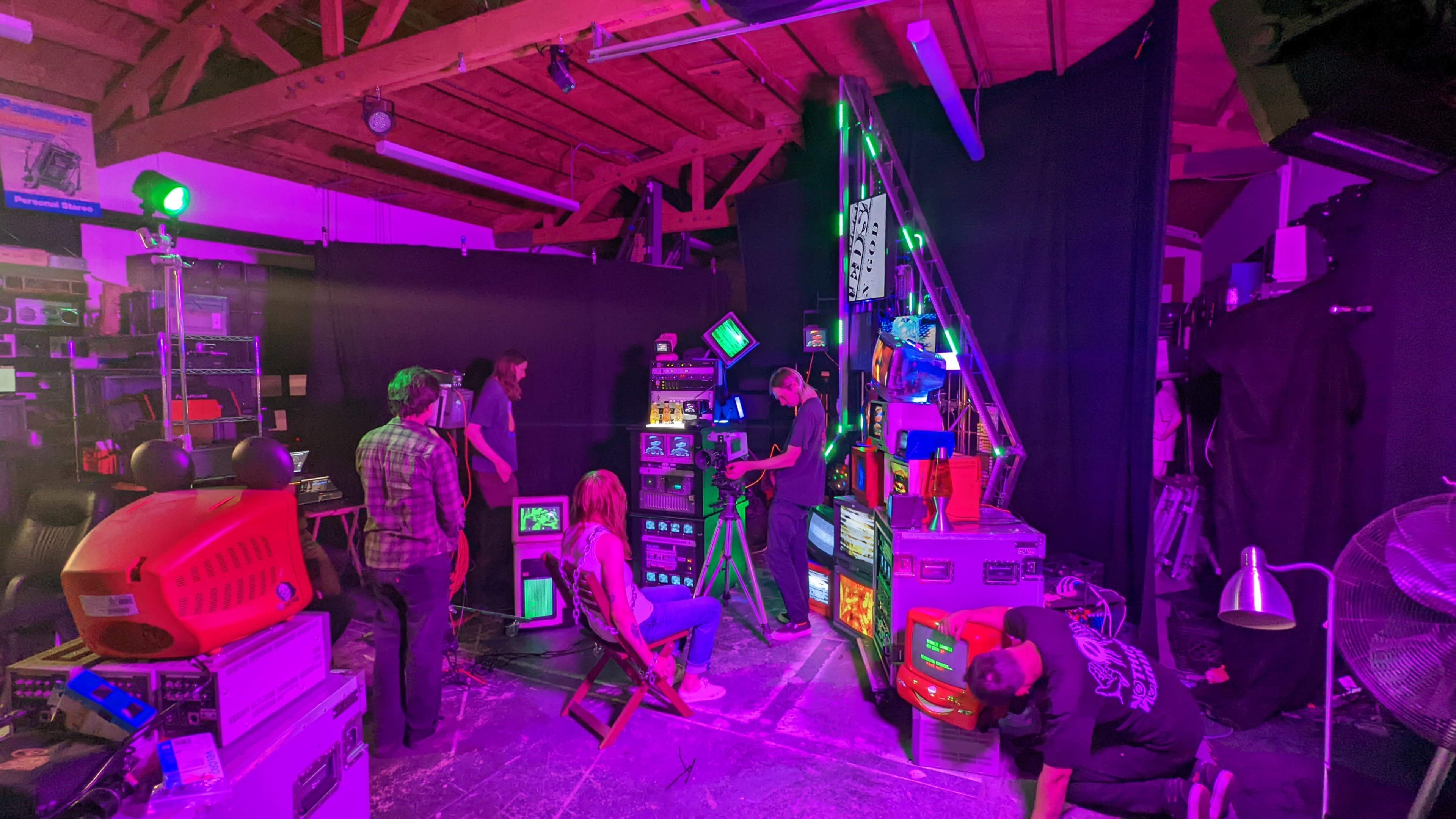 A group of people is setting up a display of vintage televisions and lighting equipment in a dimly lit studio space.