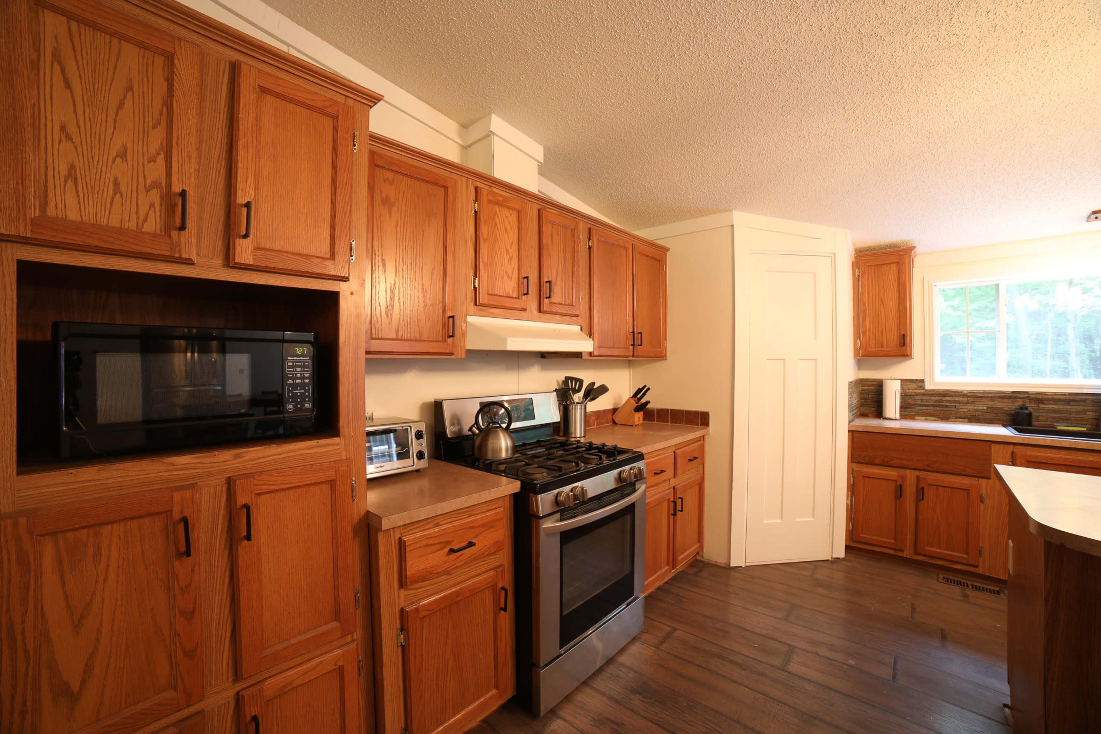 A kitchen with wooden cabinets, a stainless steel stove, a microwave, and a window letting in natural light.