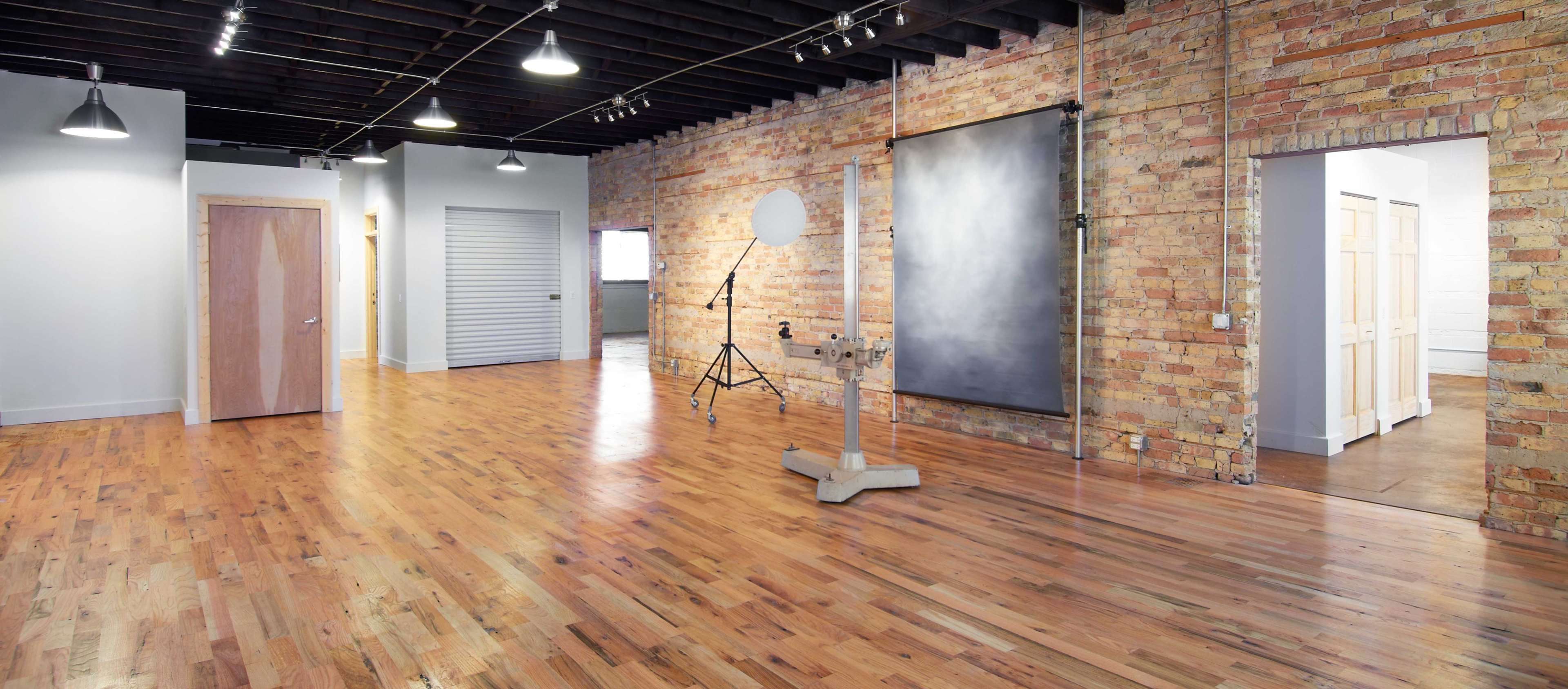 A spacious, well-lit room with wooden floors, exposed brick walls, and several doors leading to other areas.