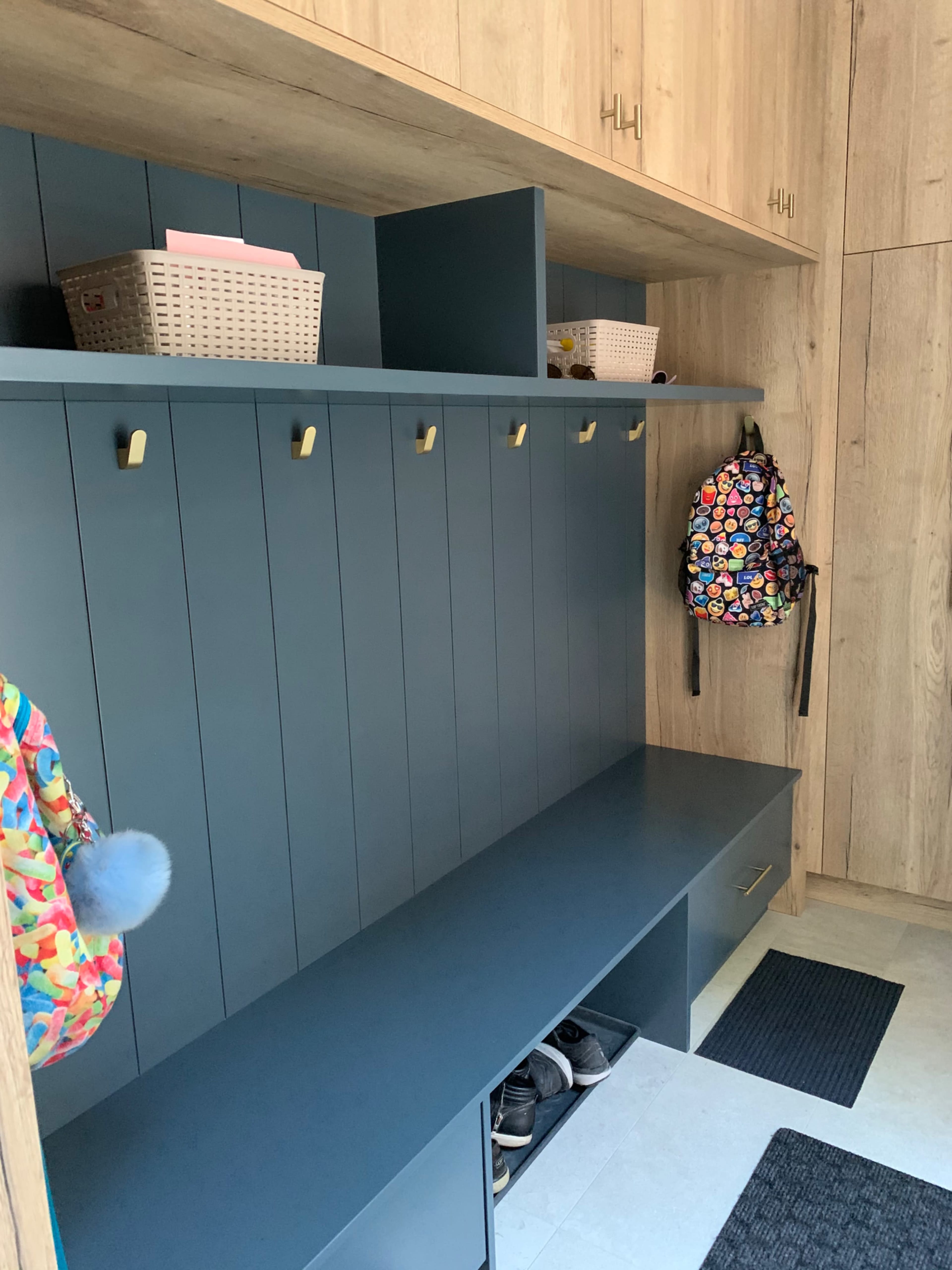 A modern entryway with a dark blue bench, vertical paneling, storage bins, hooks, and backpacks hanging on the wall.