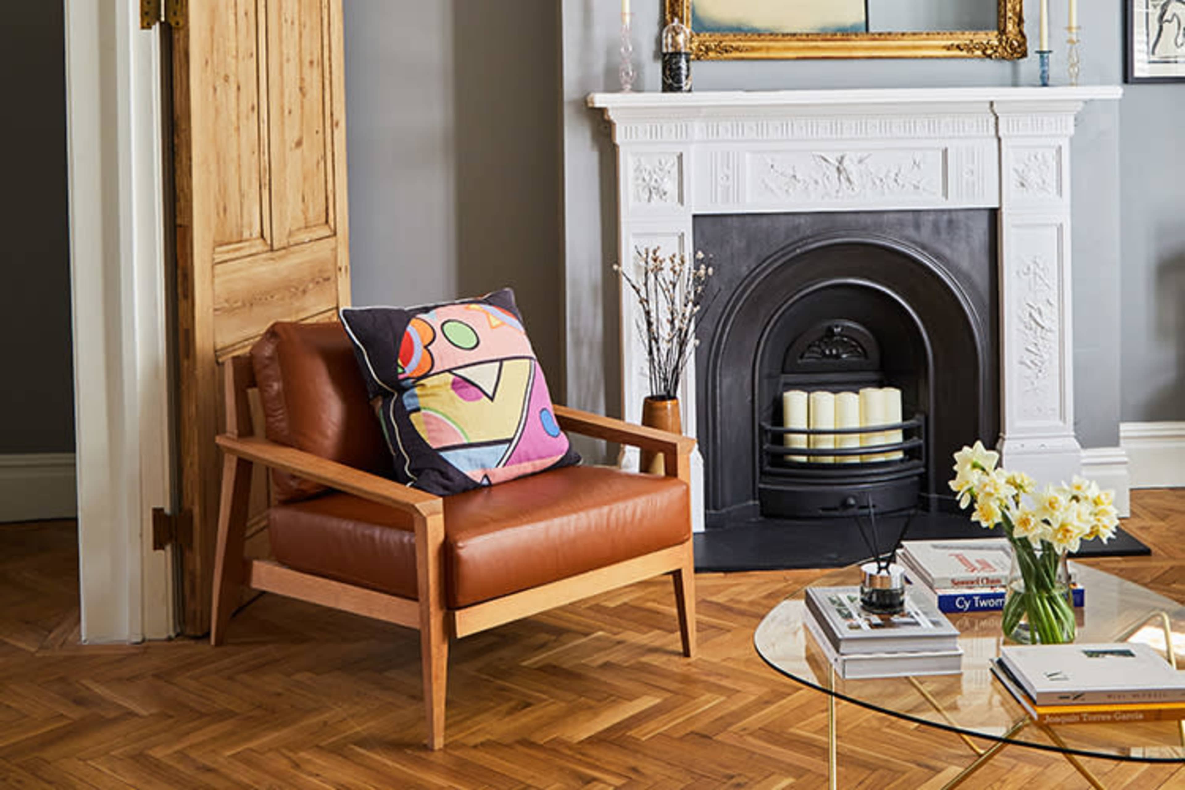 A leather armchair with a colorful patterned pillow is positioned near a fireplace in a well-decorated living room.
