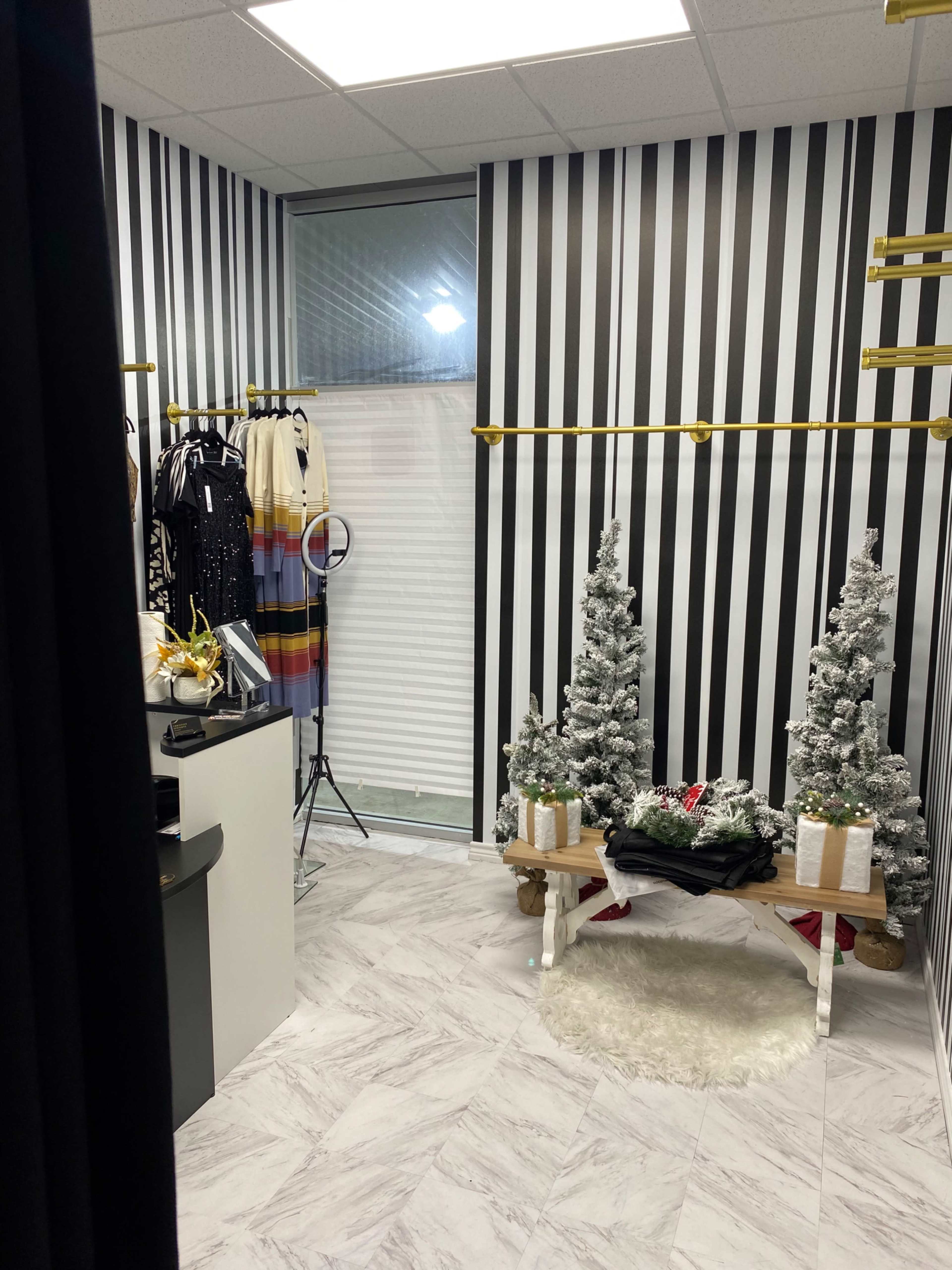 The image shows a small boutique interior featuring striped walls, two artificial Christmas trees, and a display table with holiday decorations.
