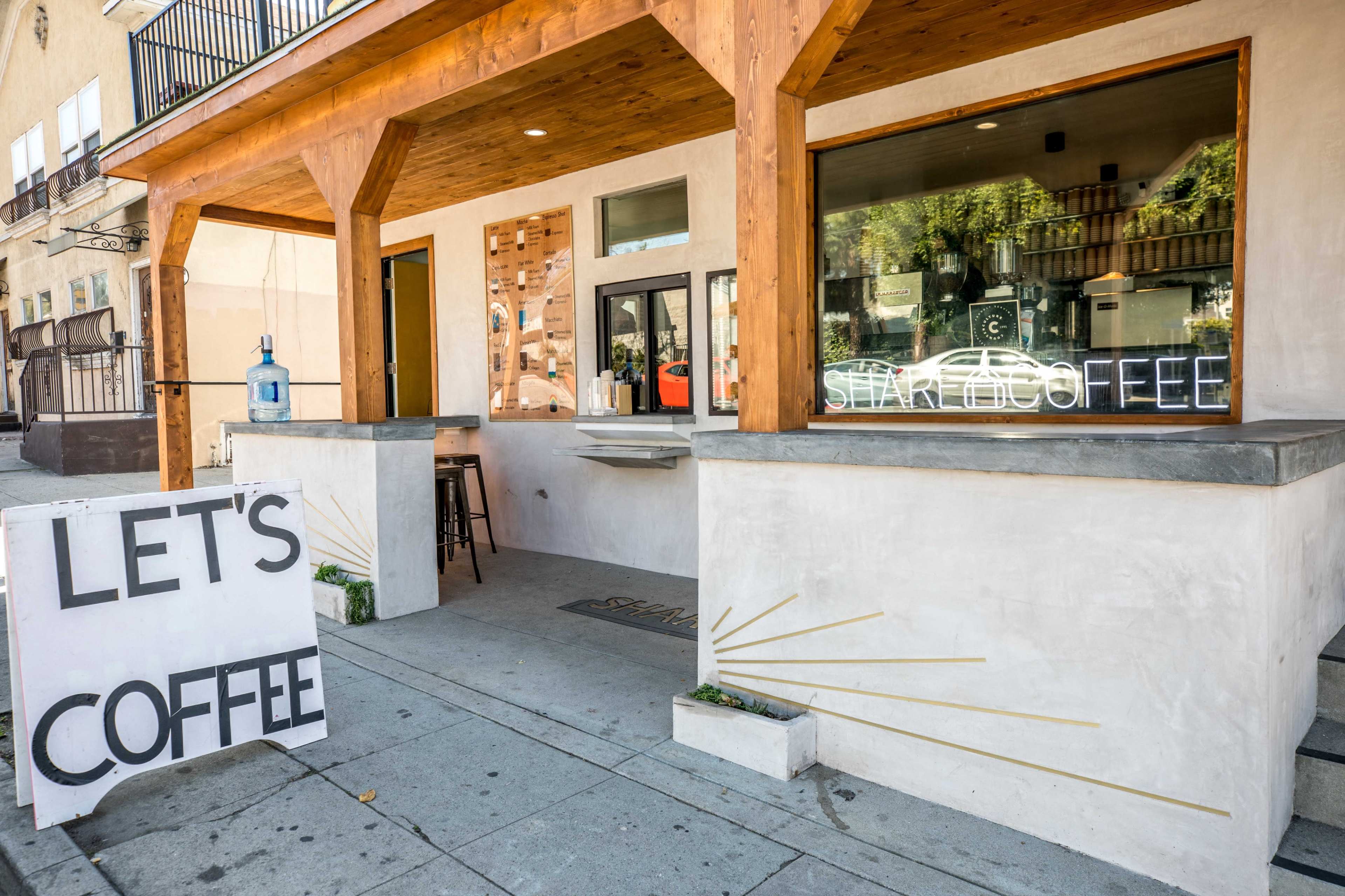 A coffee shop with a wooden overhang features an open window and a sign reading "LET'S COFFEE" outside.