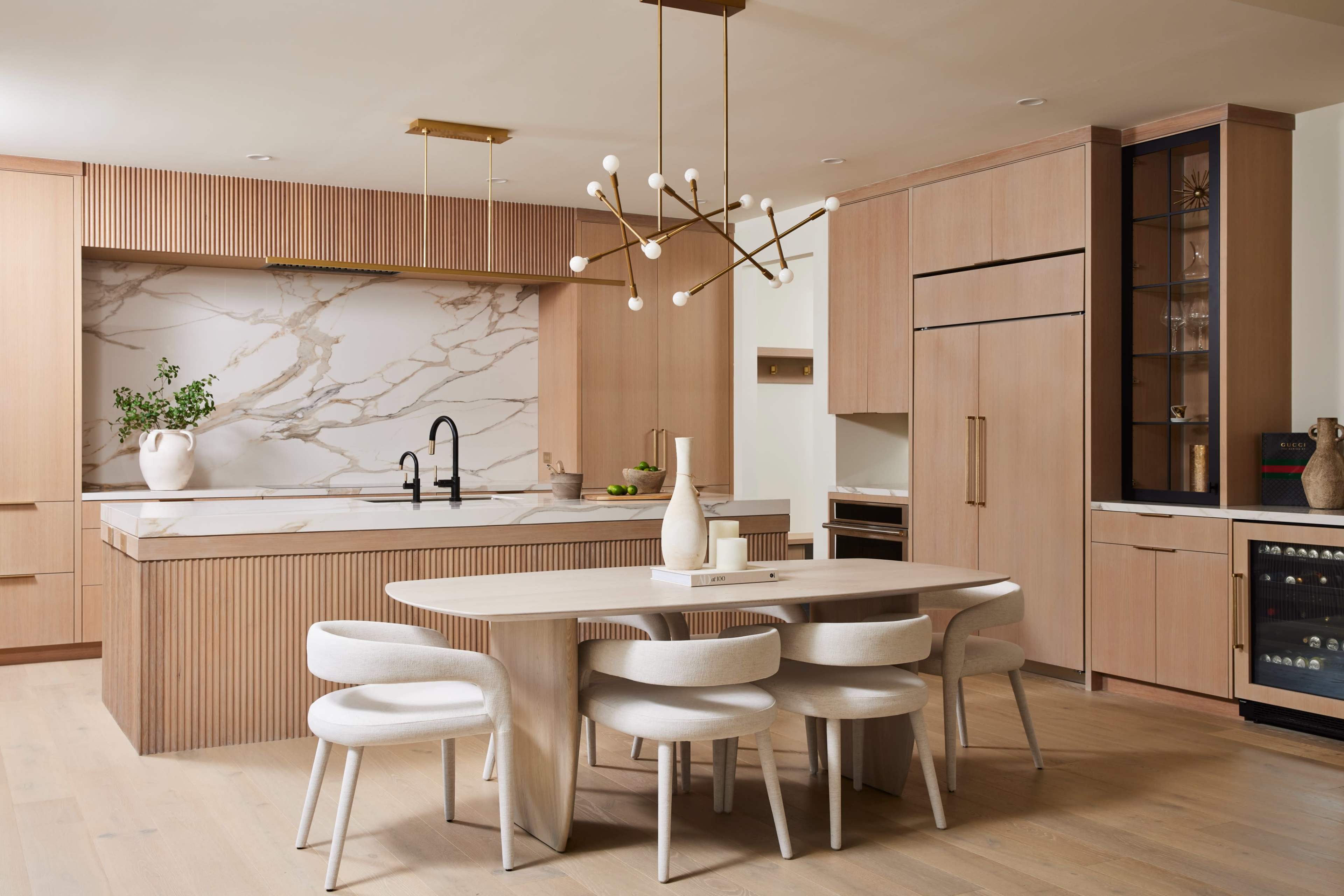 A modern kitchen with a marble countertop, wooden cabinetry, and a round dining table surrounded by upholstered chairs.