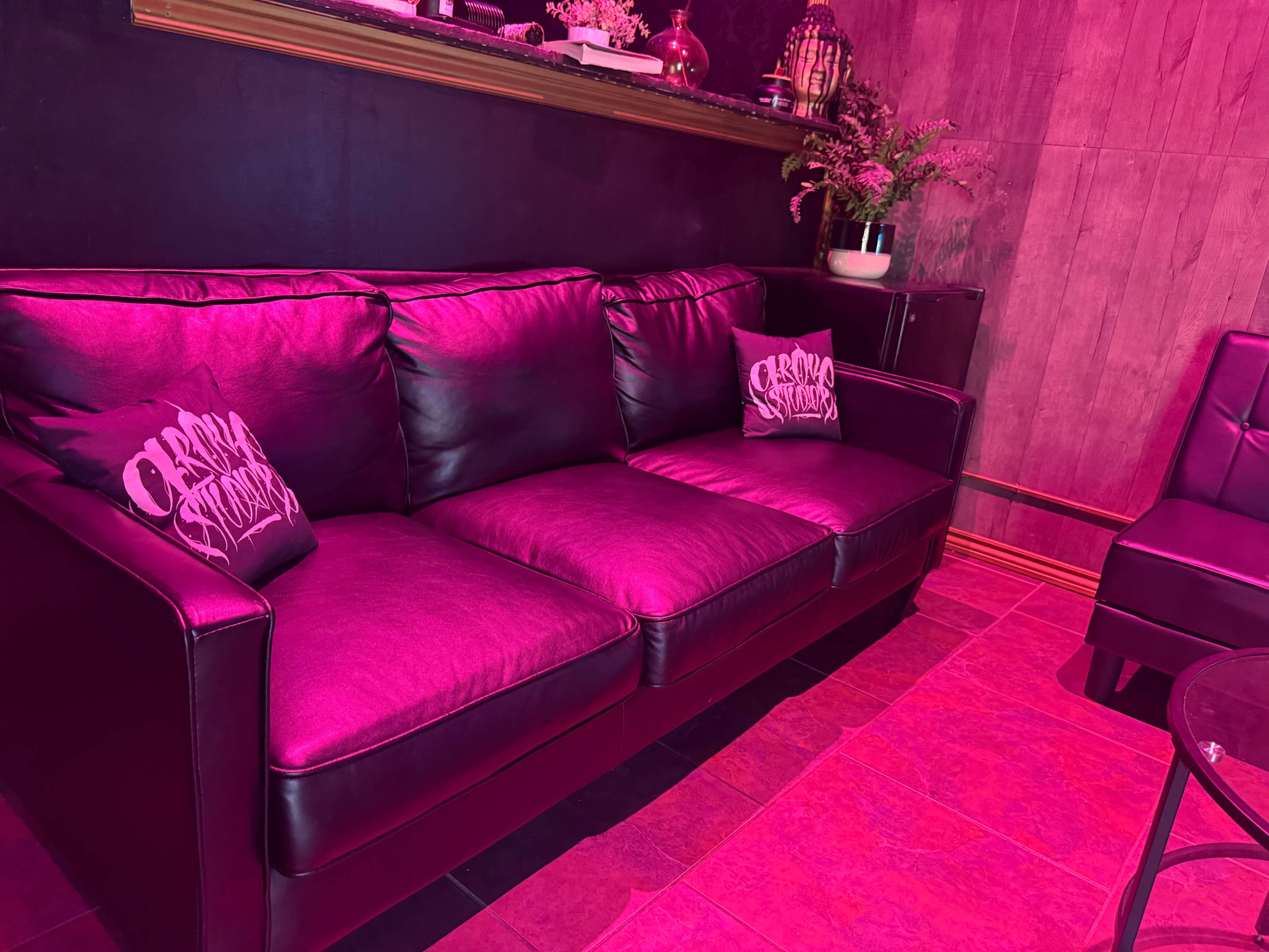 A dark room features a black leather sofa with decorative pillows and a small table beside it.