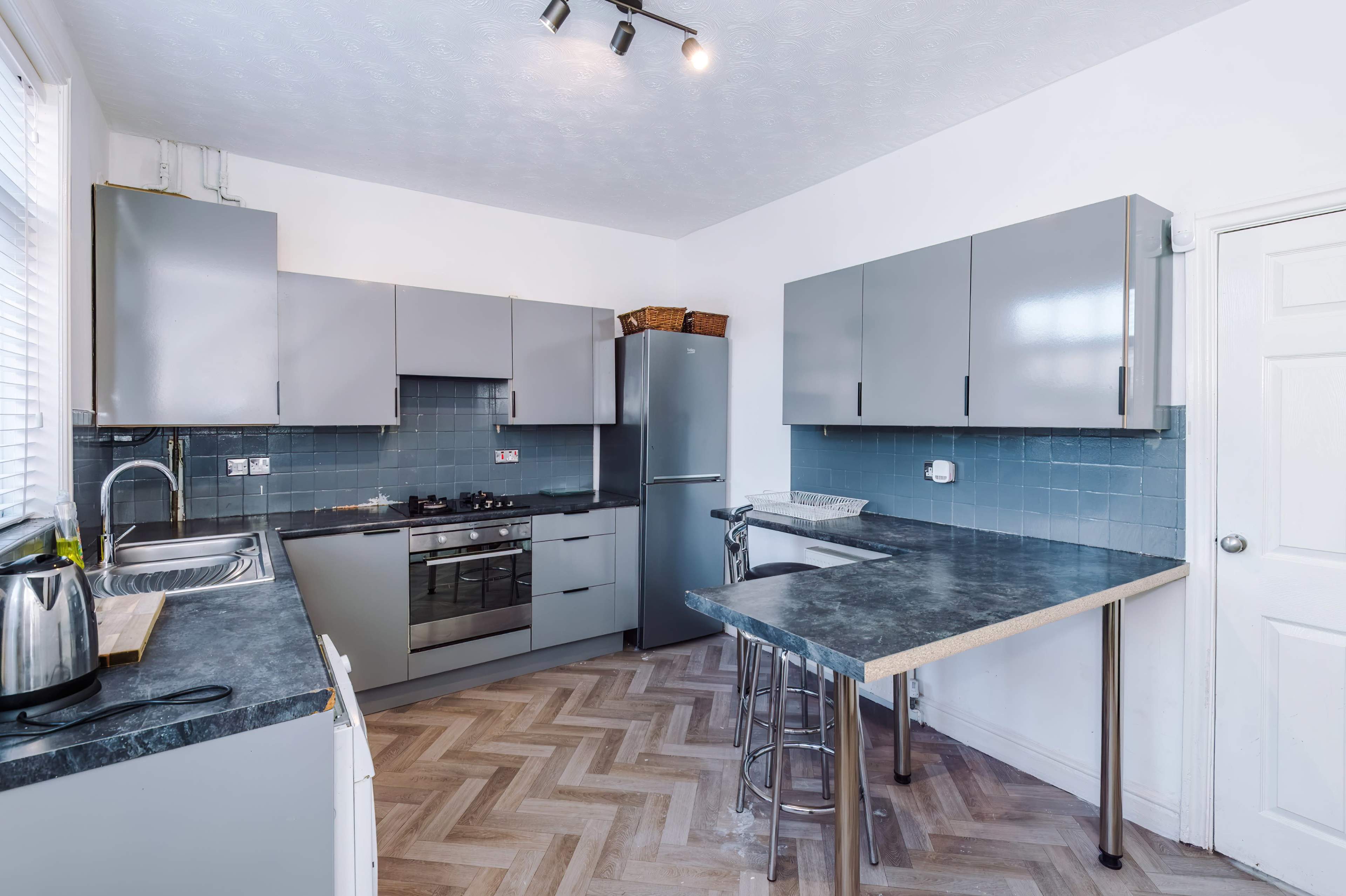 The image shows a modern kitchen with gray cabinets, a stainless steel refrigerator, and a two-tiered countertop.