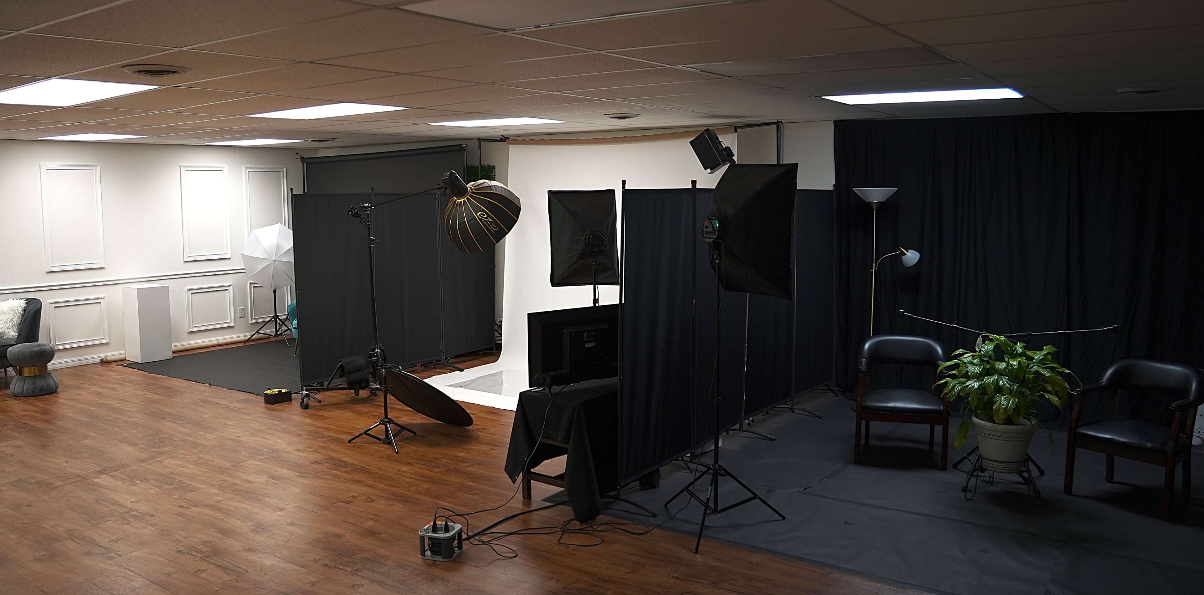 The image shows a photography studio with various lighting setups, backdrops, and seating areas.