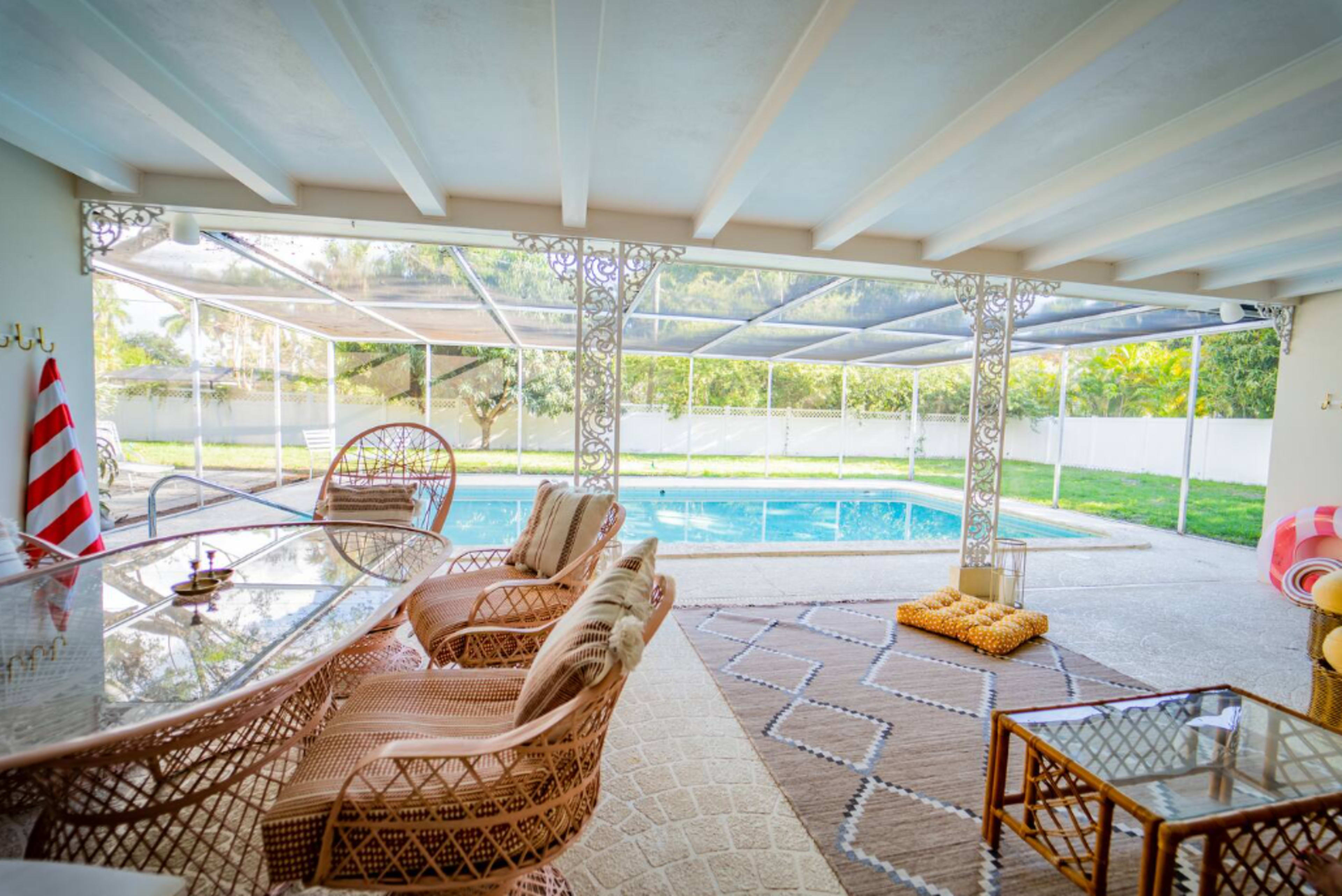 The image shows a cozy outdoor seating area overlooking a swimming pool, enclosed by a screened patio.