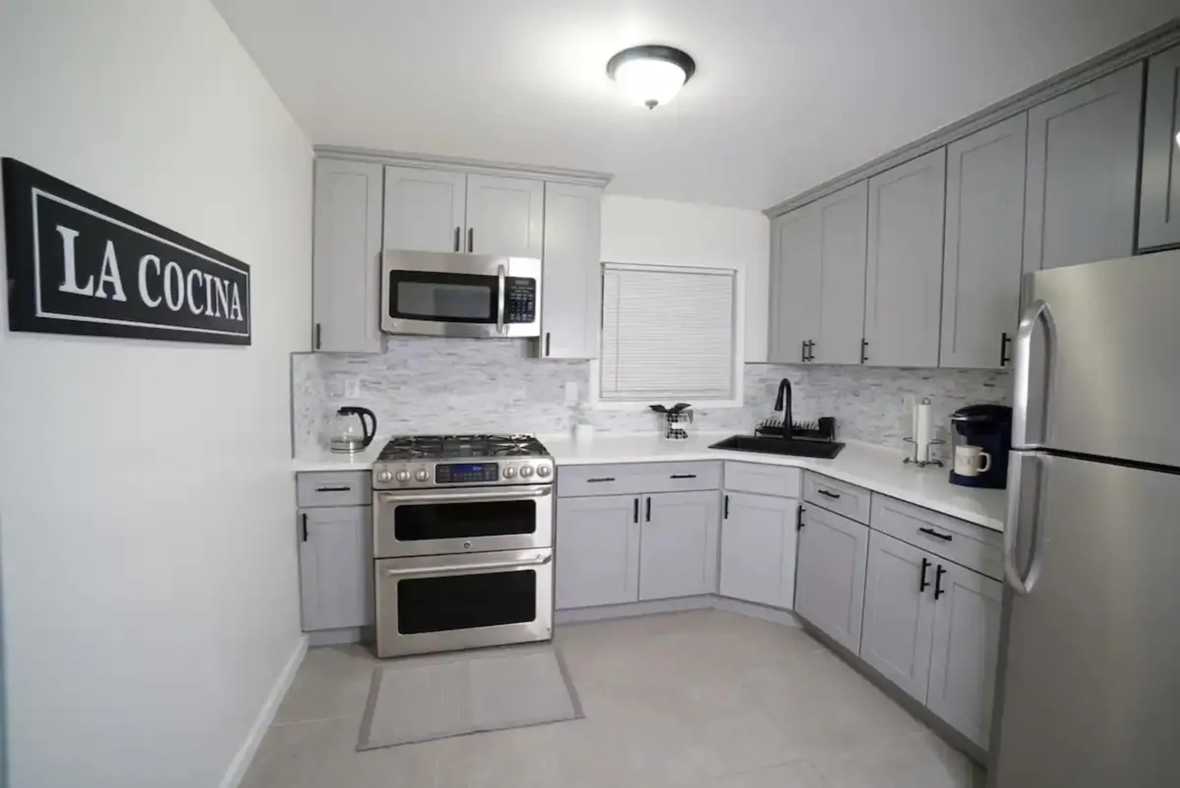 A modern kitchen featuring gray cabinetry, stainless steel appliances, and a white countertop with a tile backsplash.
