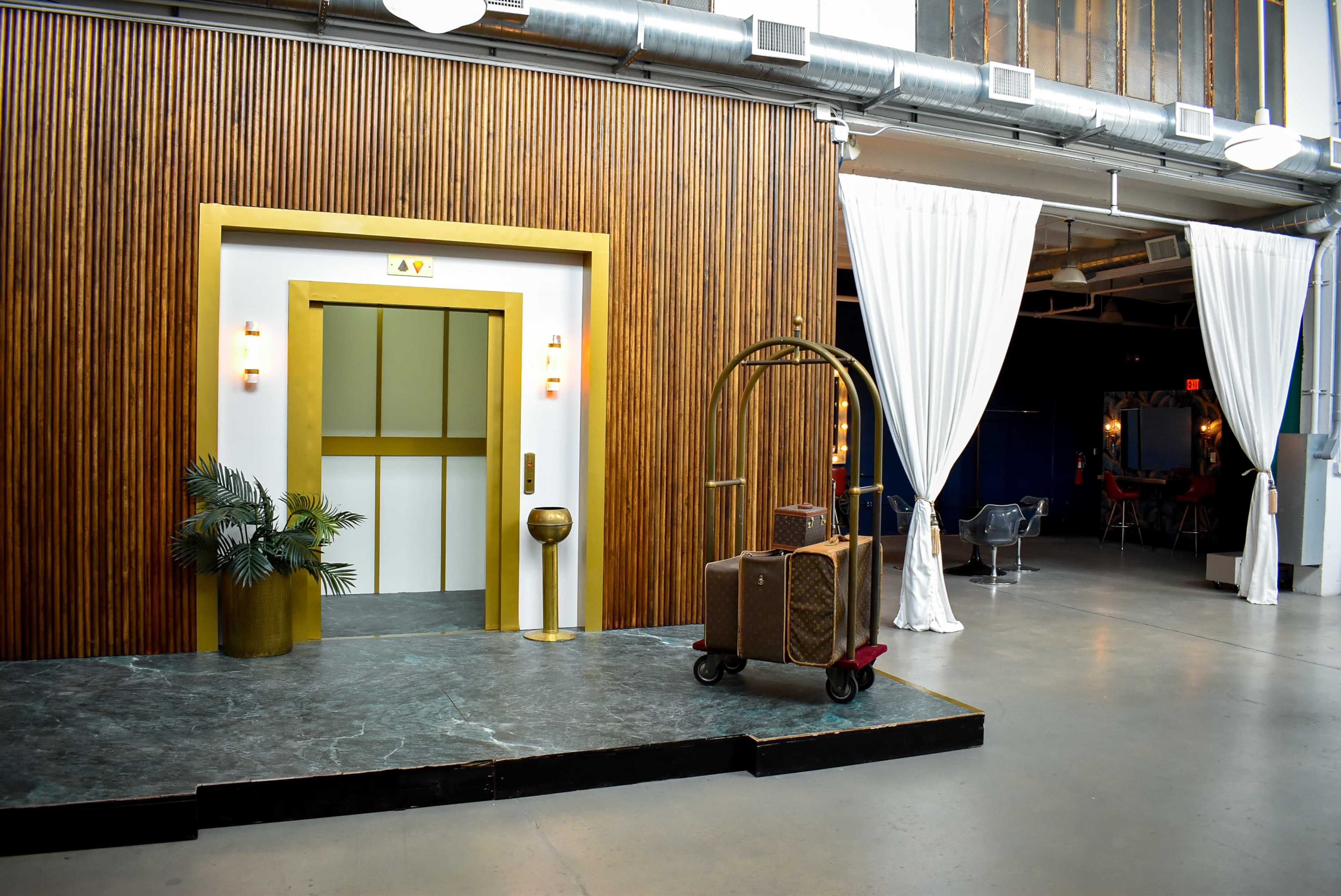 A stylish elevator area with a luggage cart positioned in front of it, surrounded by wooden paneling and draped curtains.