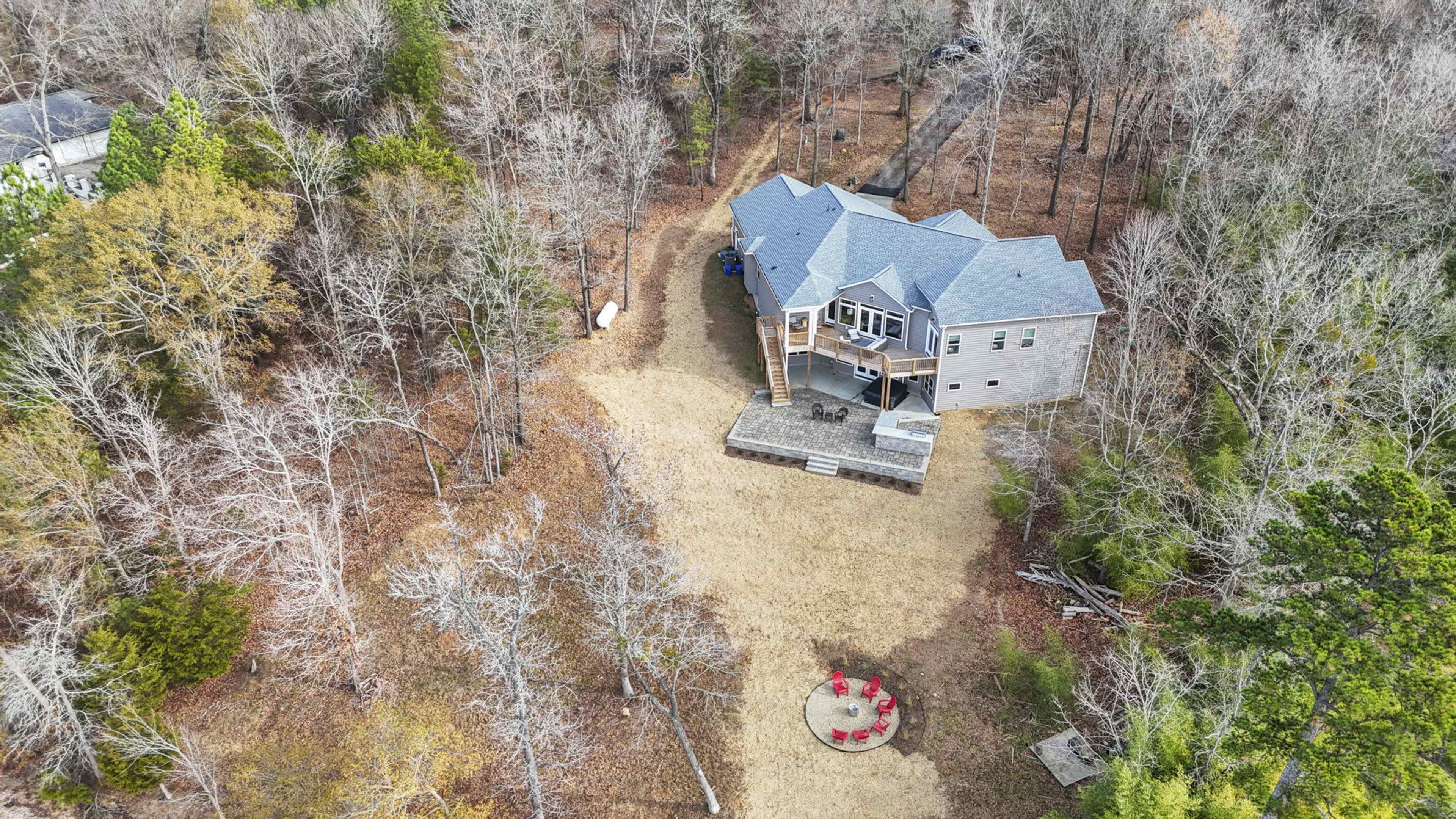 A large gray house sits in a clearing surrounded by bare trees and patches of grass.