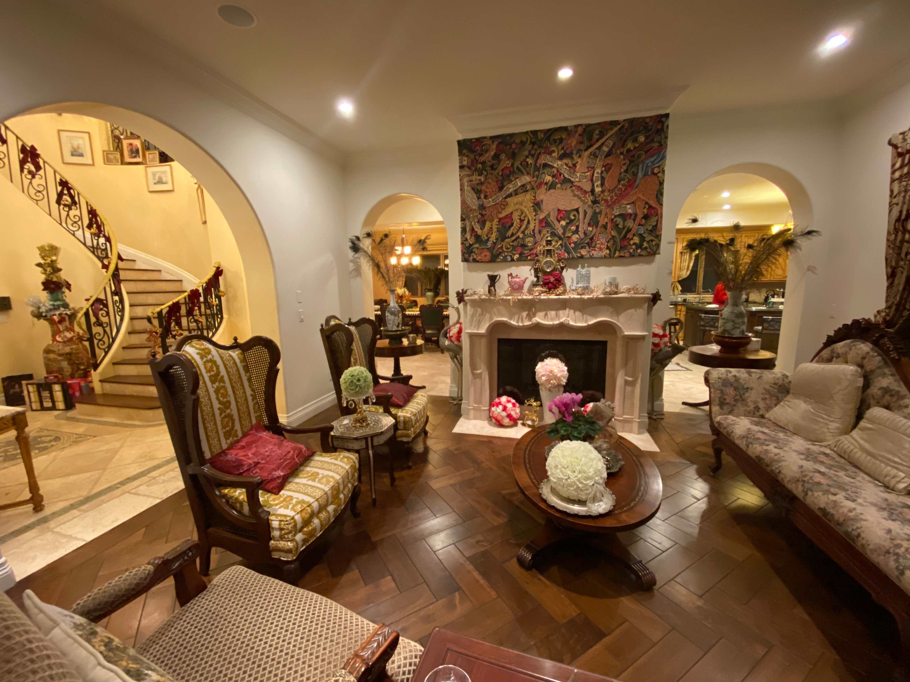 The image shows a elegantly decorated living room with arched doorways, a fireplace, and ornate furniture, featuring a staircase in the background.