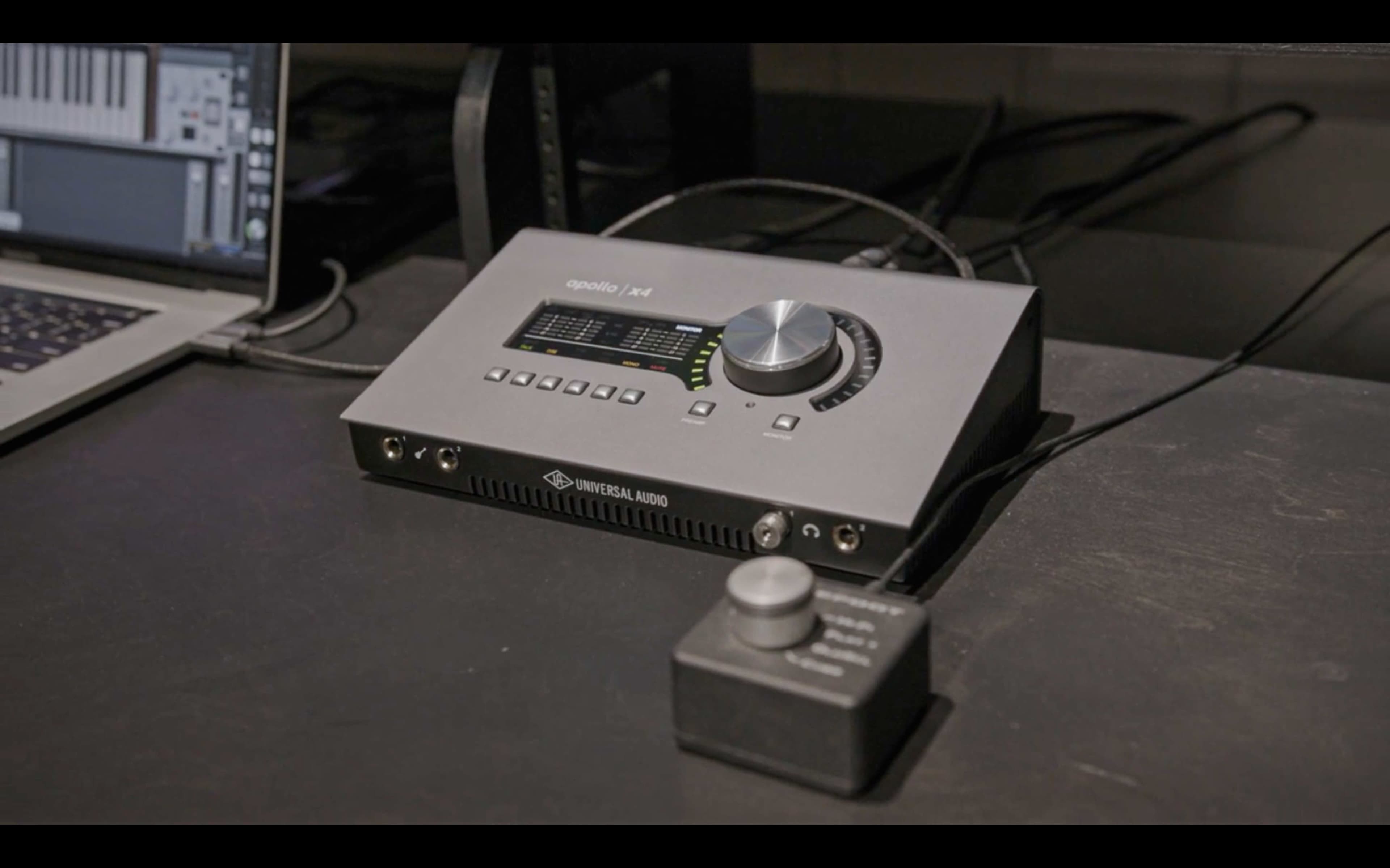 A Universal Audio Apollo Twin audio interface sits on a black table, connected to a computer and featuring multiple input and output controls.